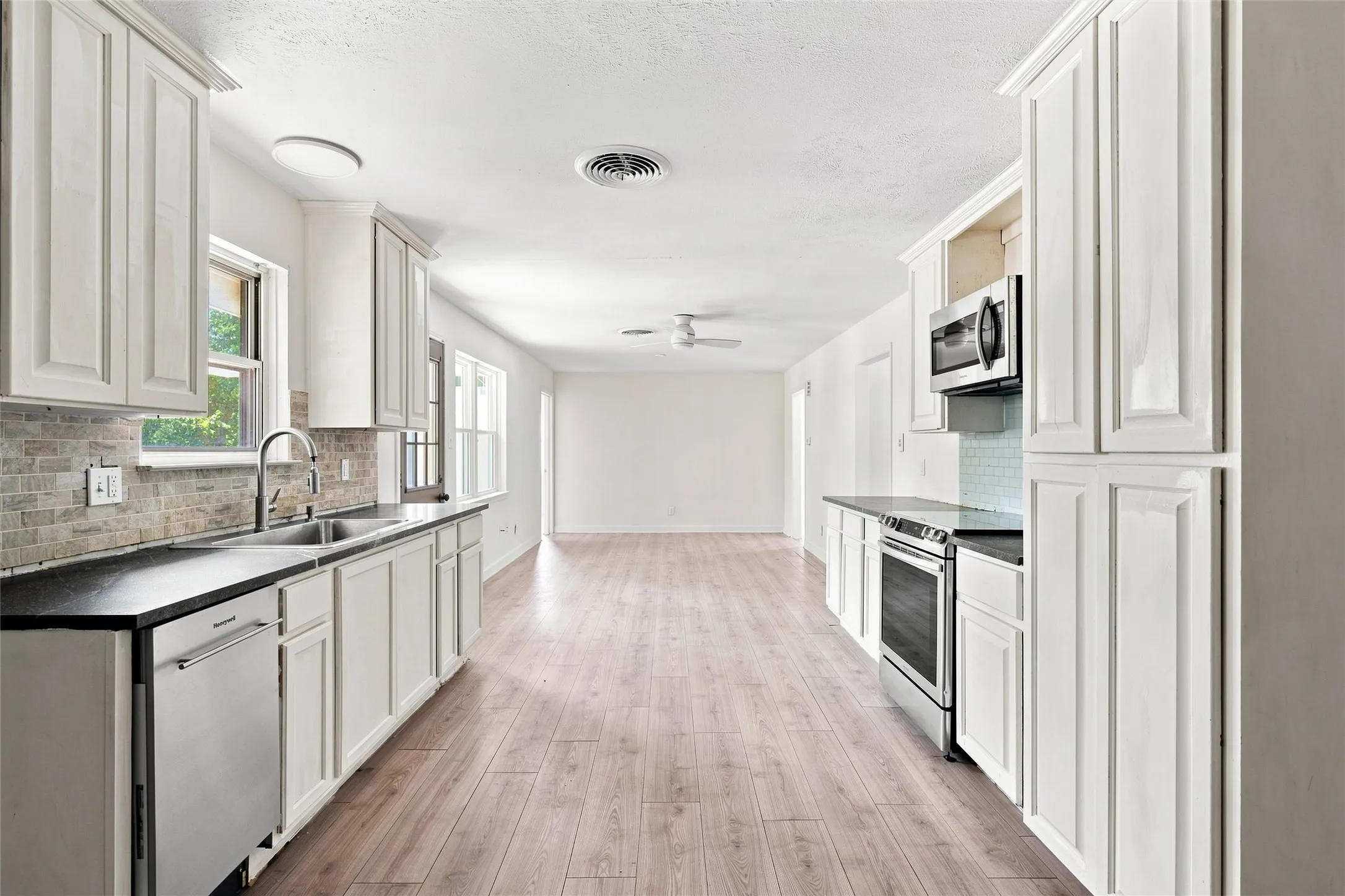 Kitchen featuring white cabinetry, dark countertops, a mosaic tile backsplash, stainless steel appliances, and wood-finish flooring