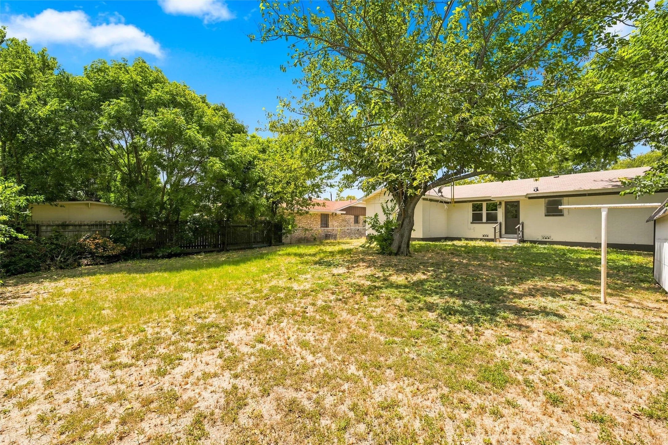 Expansive backyard with a mature tree, privacy fencing, and a rear exterior with a patio door