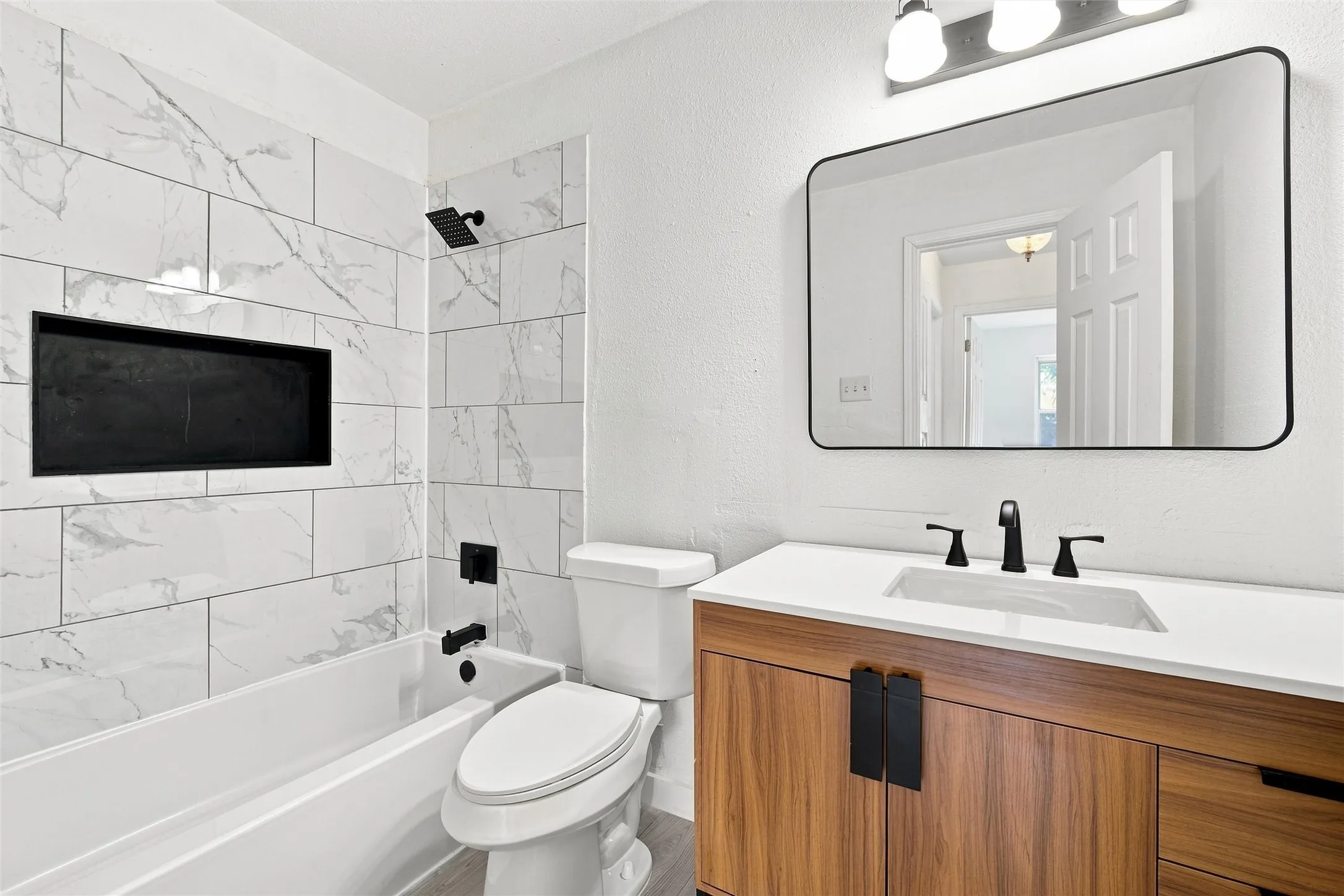 Contemporary bathroom featuring a wood-finish vanity with integrated sink and countertop, matte black hardware, and a framed mirror with metal trim