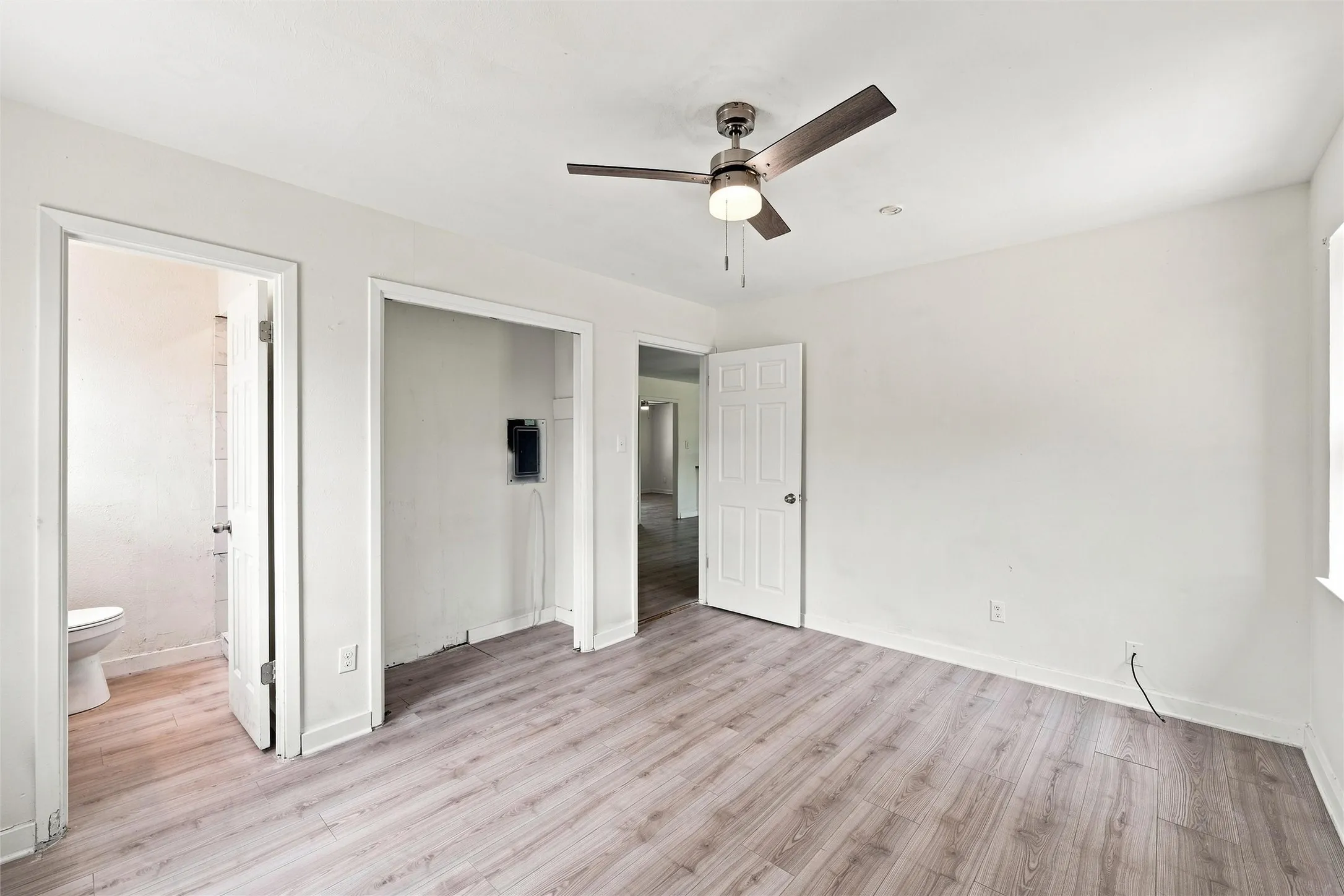 Spacious room featuring wood-finish flooring, a ceiling fan with integrated lighting, and white interior doors