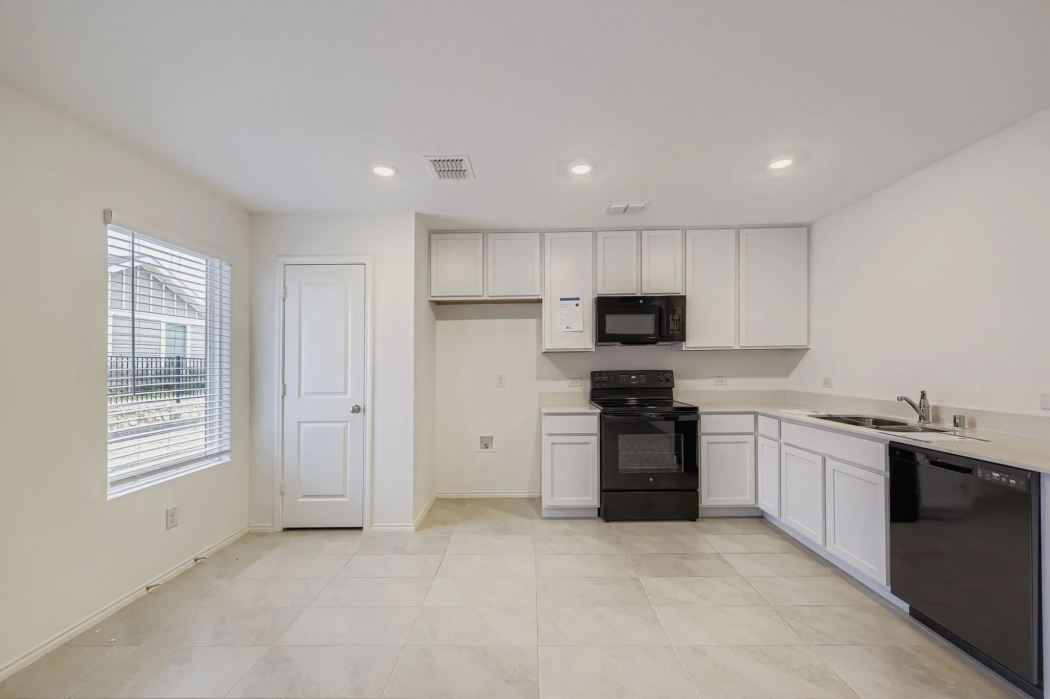 White cabinetry with black appliances, tile flooring, recessed lighting, and a window with horizontal blinds