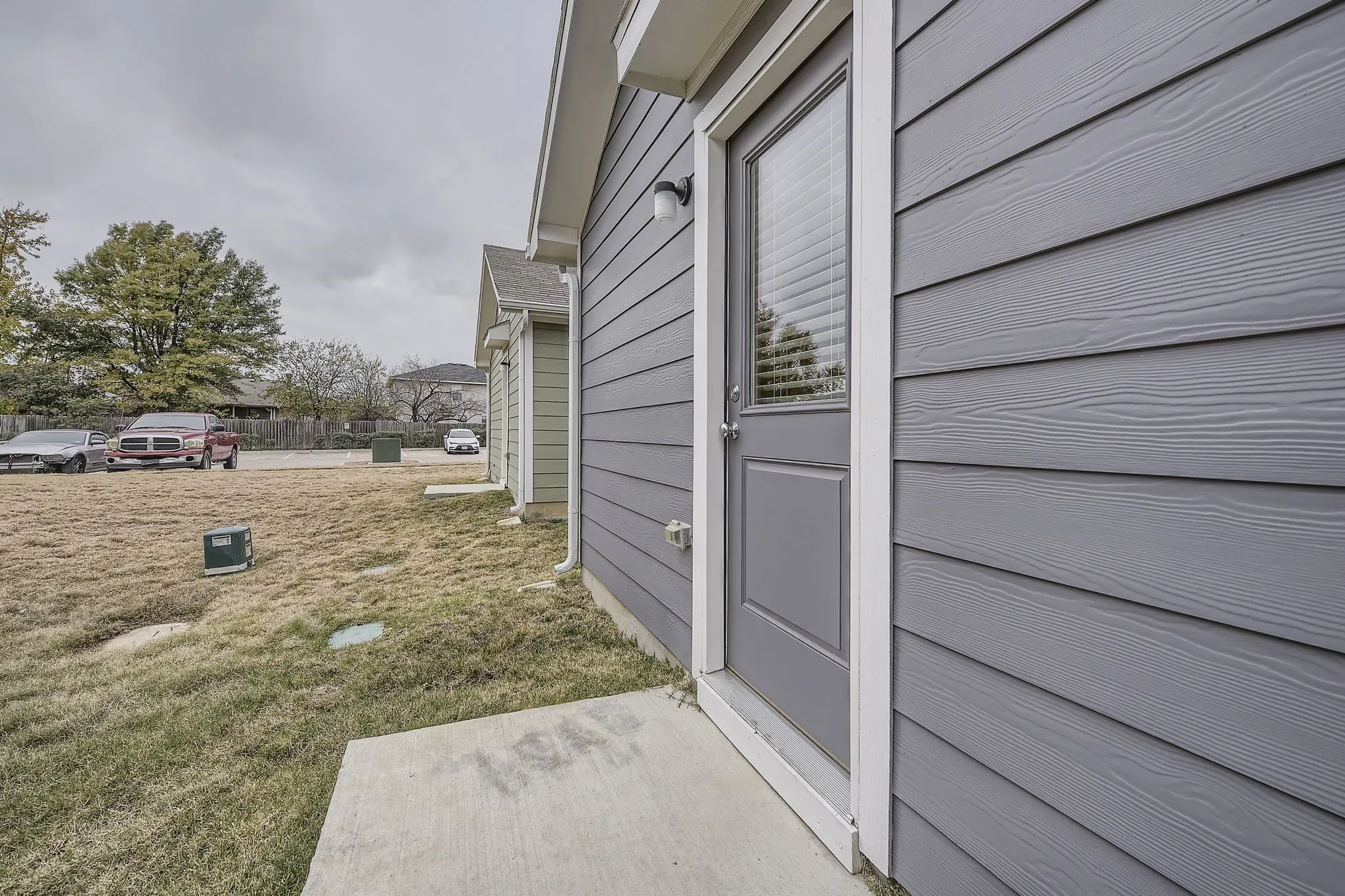 Gray horizontal siding, white trim around door and windows, concrete walkway, and exterior lighting fixture