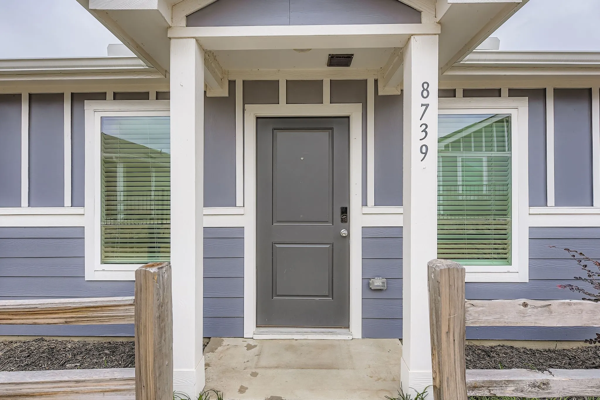 Front entry featuring vertical house numbers, a grey paneled door, and two side windows with blinds
