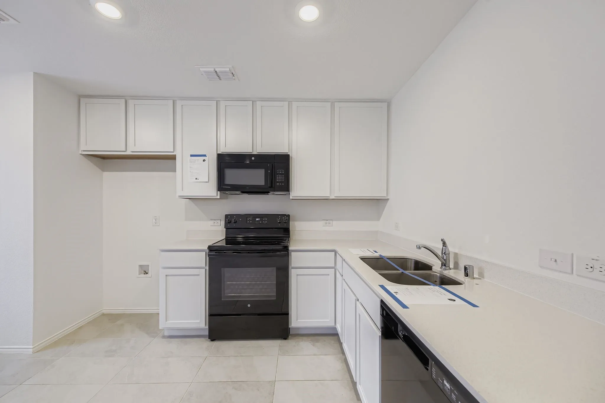 Kitchen featuring white cabinetry, light-toned countertops, a stainless steel double-basin sink, and a black range with an overhead microwave