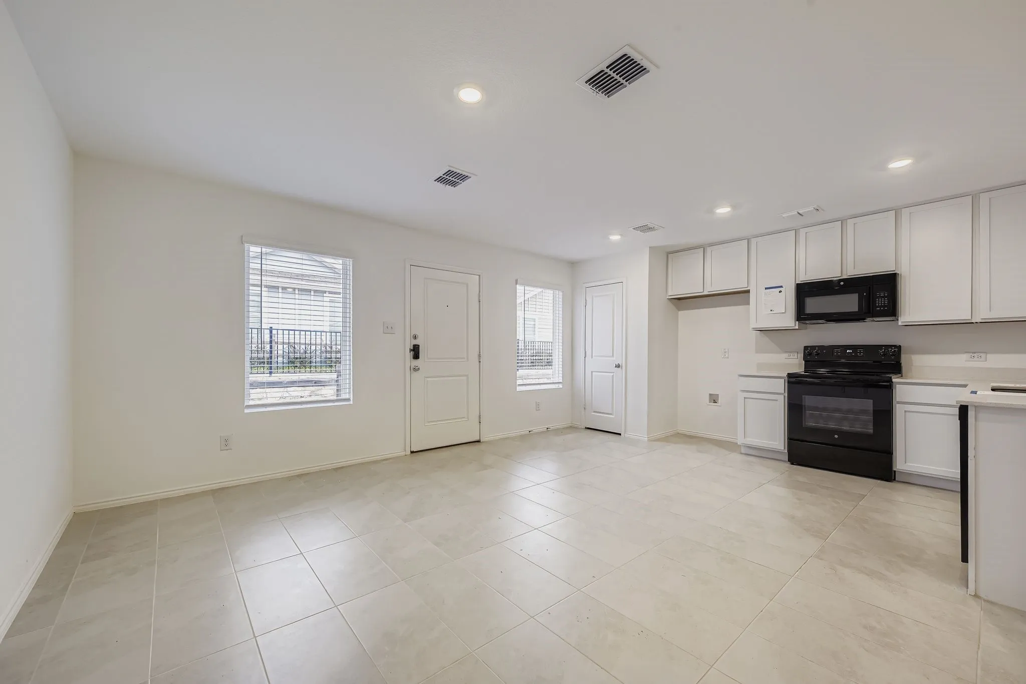 Open-concept living area with light-toned tile flooring, recessed lighting, and white walls