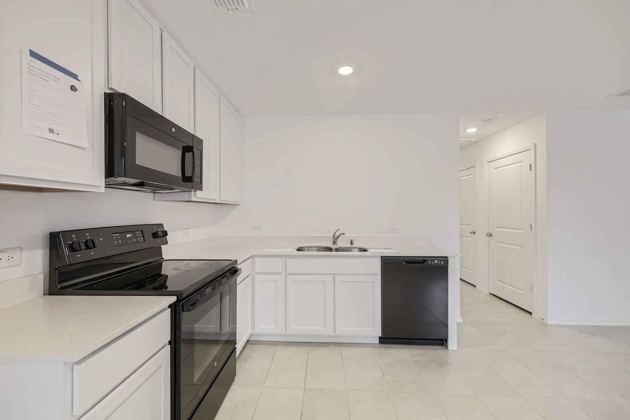 White cabinetry, light-toned countertops, tile flooring, recessed lighting, and black appliances