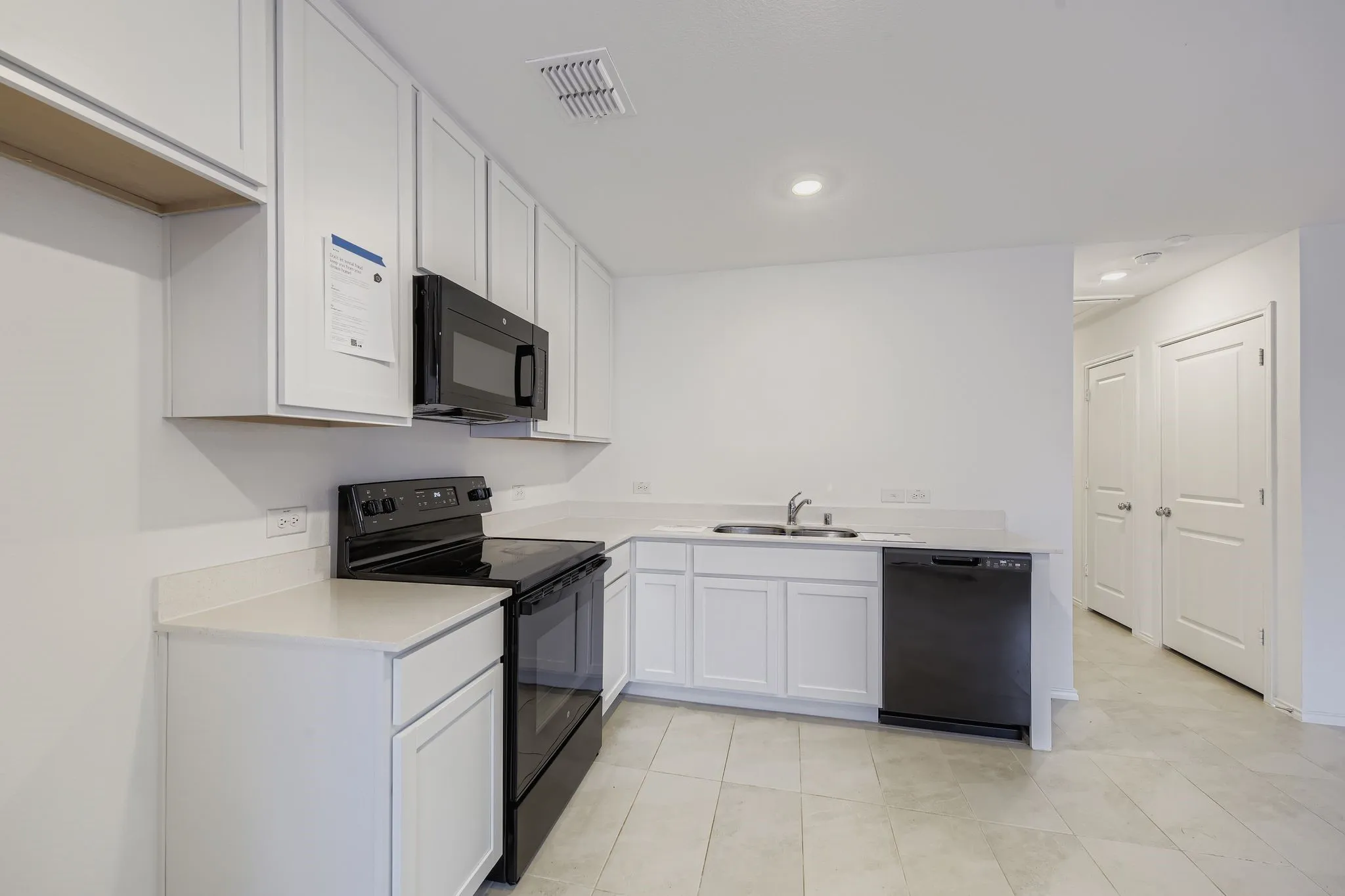 Kitchen featuring white shaker-style cabinetry, light-toned countertops, black appliances, and recessed lighting
