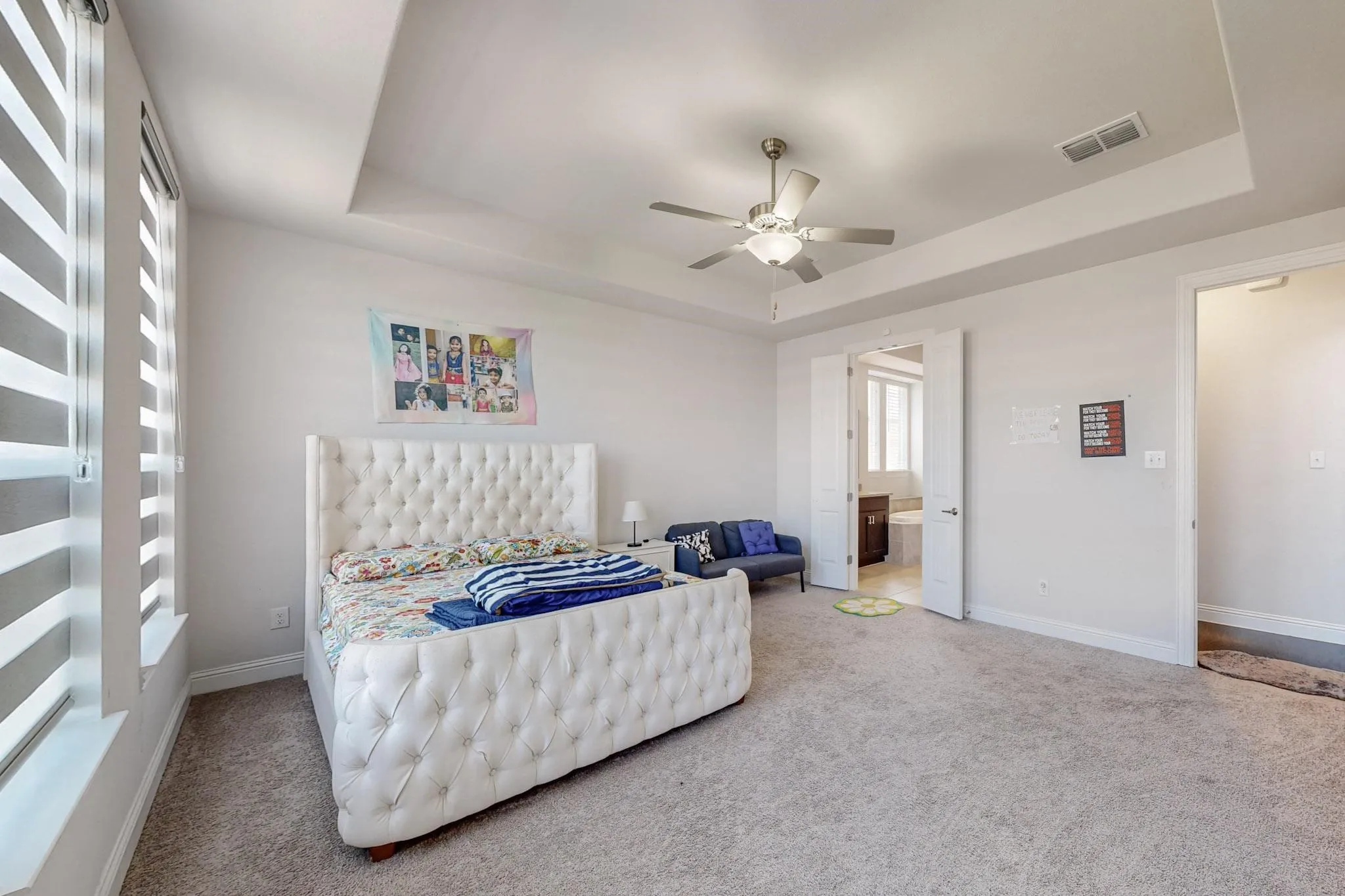 Carpeted bedroom featuring ensuite bath, ceiling fan, and a raised ceiling