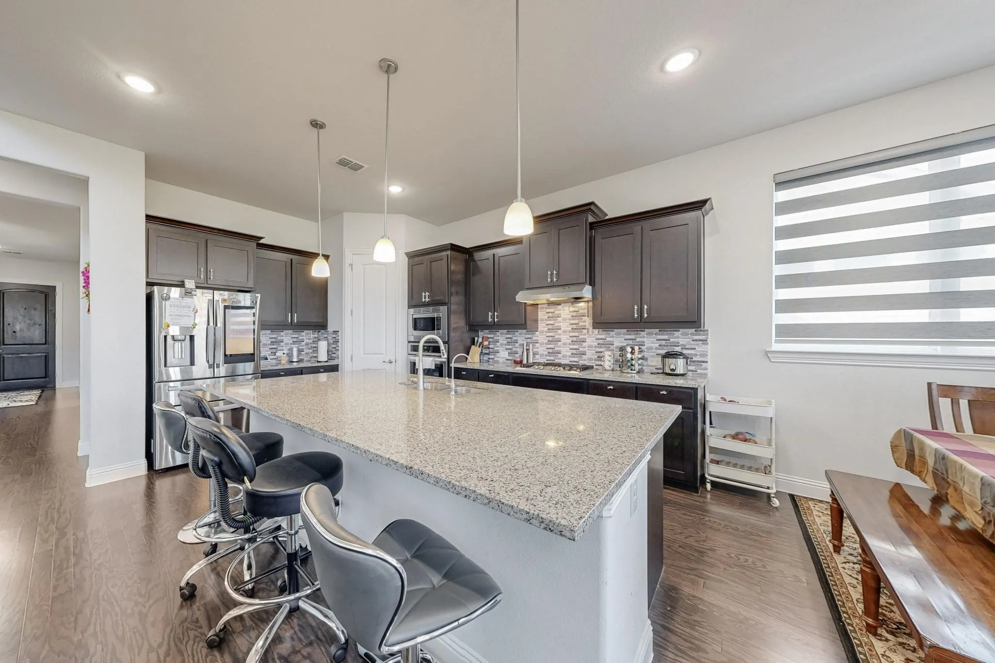 Kitchen featuring light stone countertops, dark wood-type flooring, appliances with stainless steel finishes, and hanging light fixtures