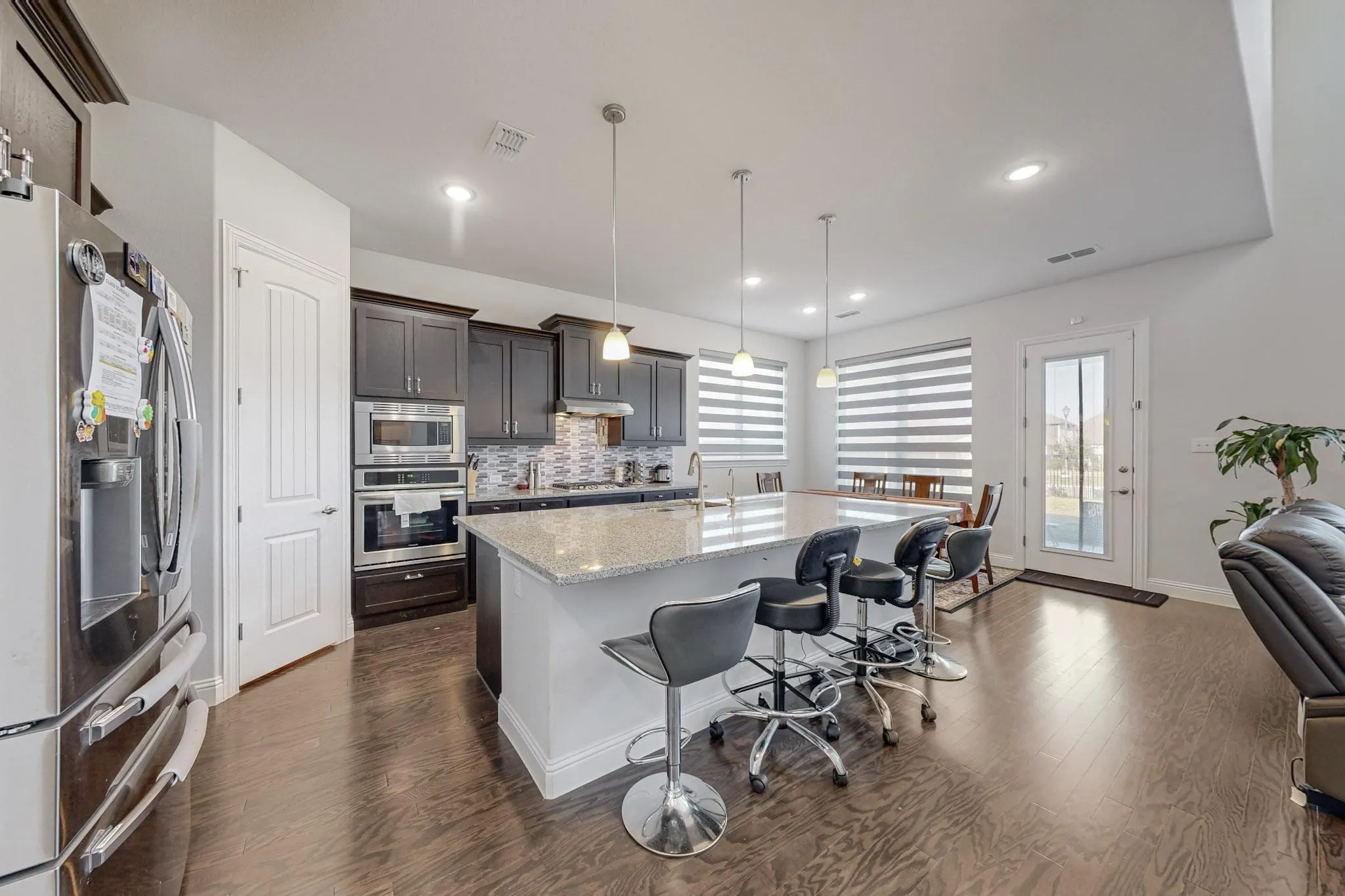 Kitchen featuring dark hardwood / wood-style flooring, appliances with stainless steel finishes, an island with sink, pendant lighting, and light stone counters