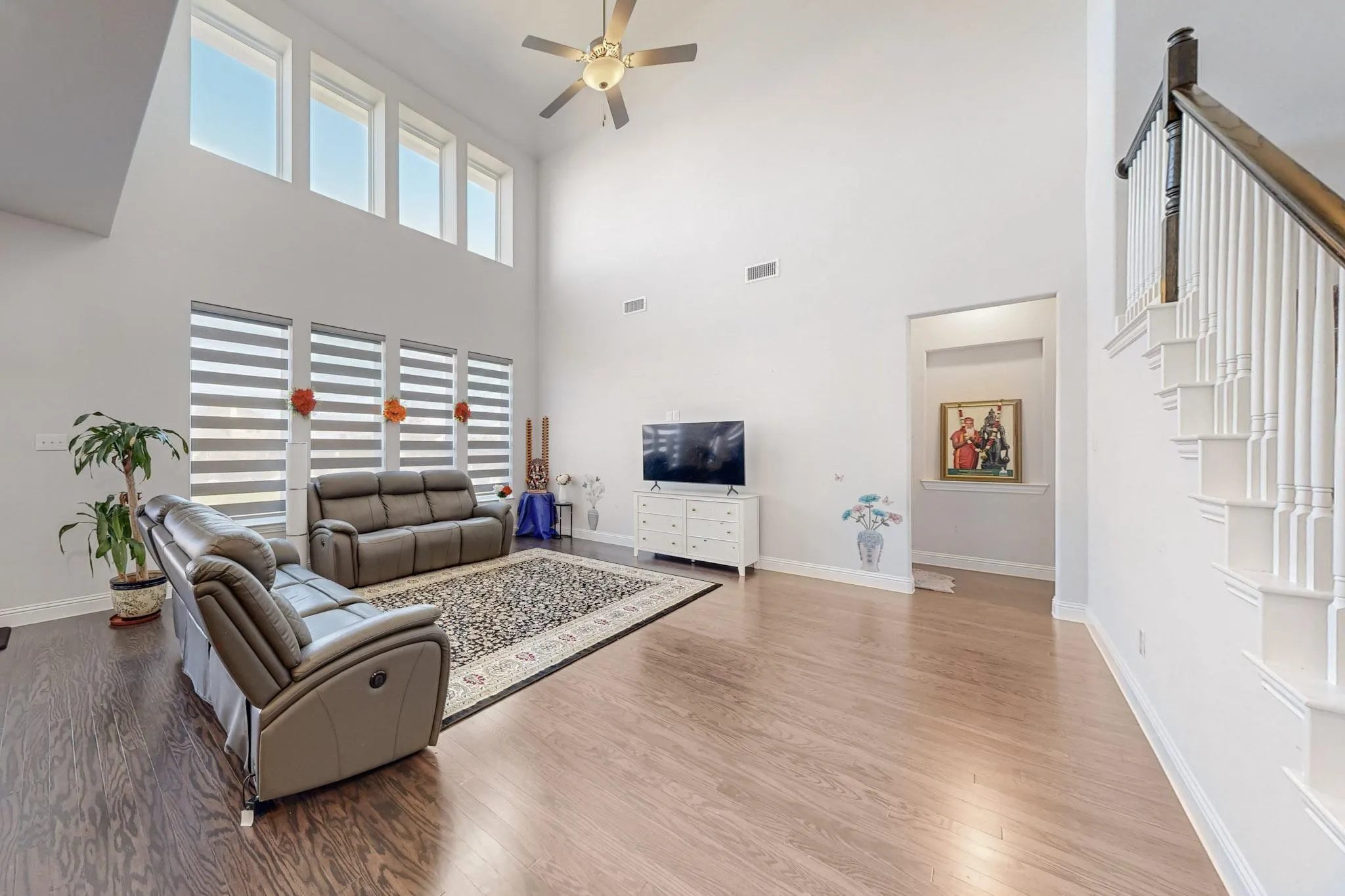 Living room featuring wood-type flooring, a high ceiling, and ceiling fan