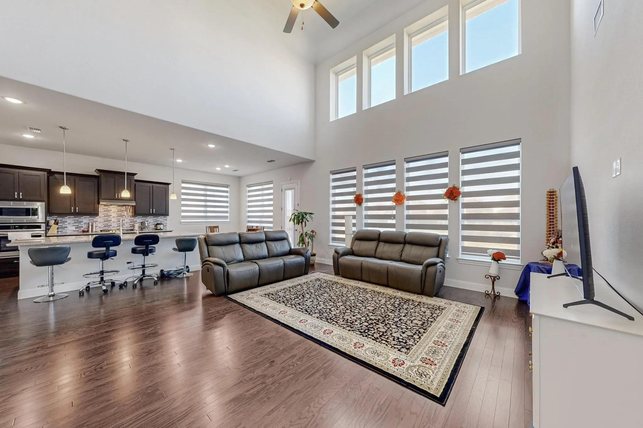 Living room with dark wood-type flooring, ceiling fan, and a high ceiling
