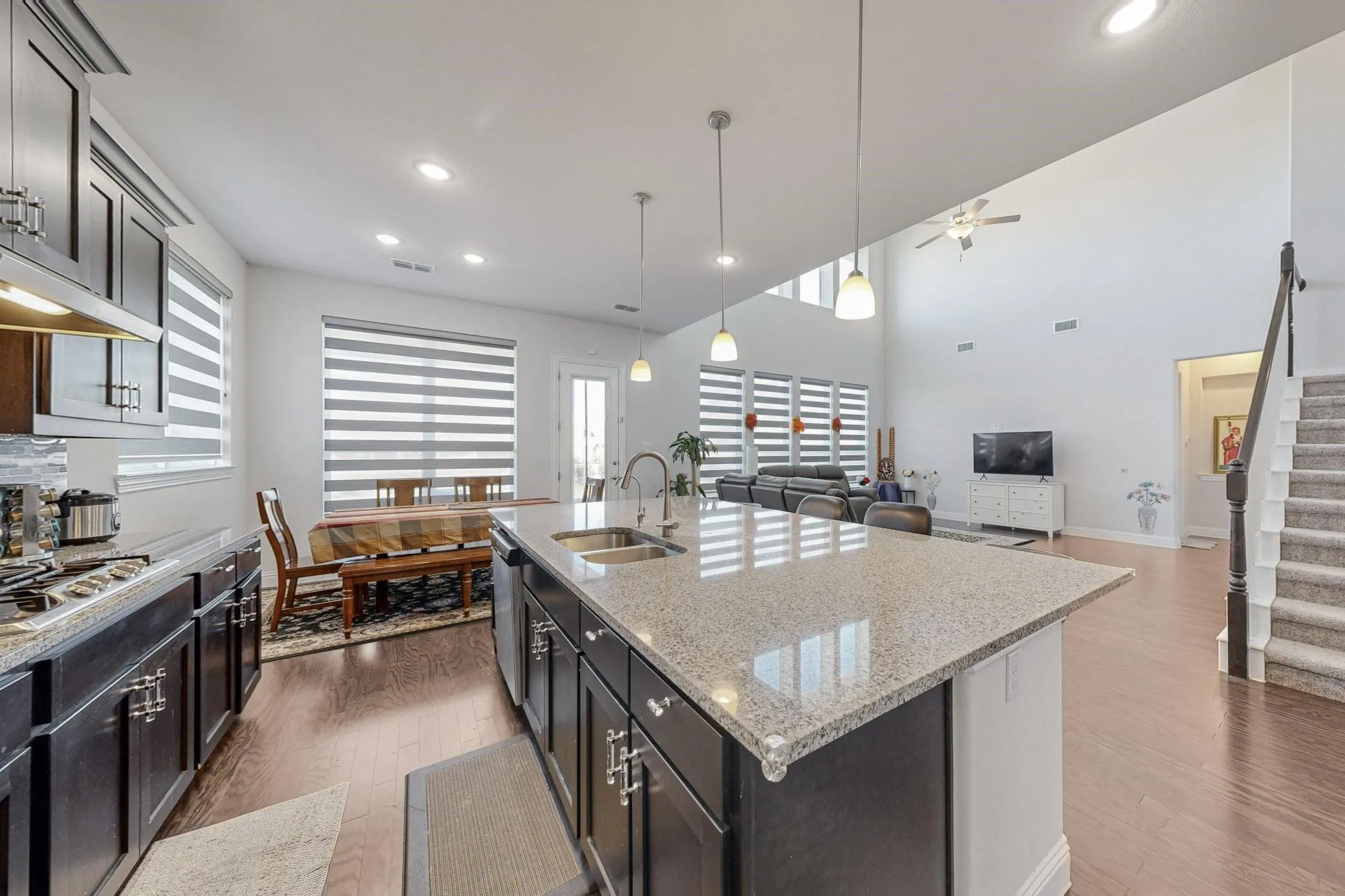 Kitchen with appliances with stainless steel finishes, sink, dark hardwood / wood-style flooring, decorative light fixtures, and a kitchen island with sink