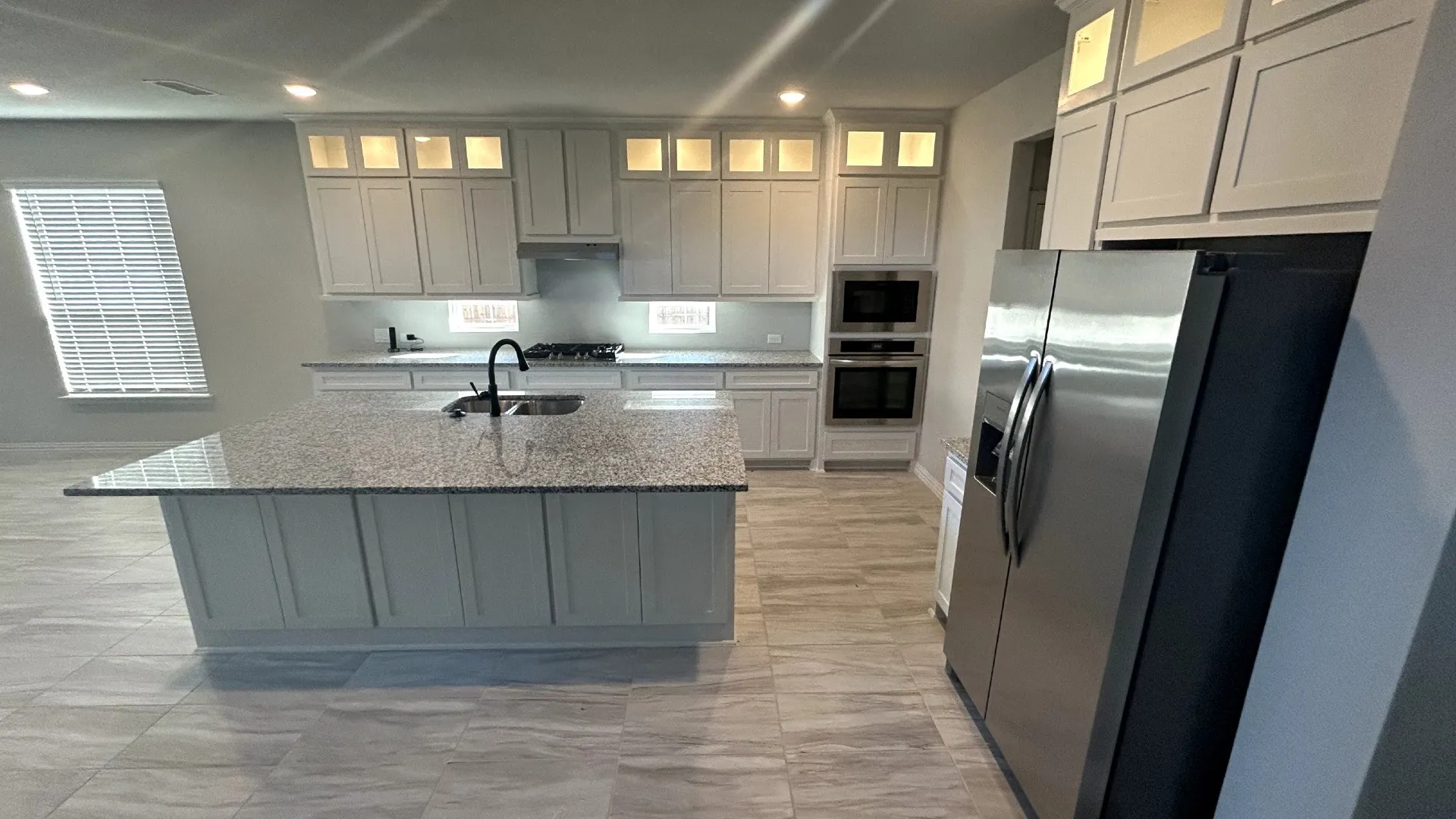 Kitchen featuring a large island with a surface, white shaker-style cabinetry, stainless steel appliances, and tile flooring