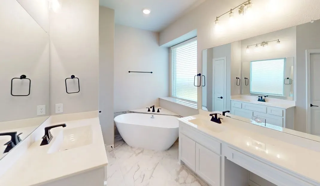 White freestanding soaking tub, dual vanity with undermount sinks, stone-finish countertops, matte black plumbing fixtures, and marble-look tile flooring