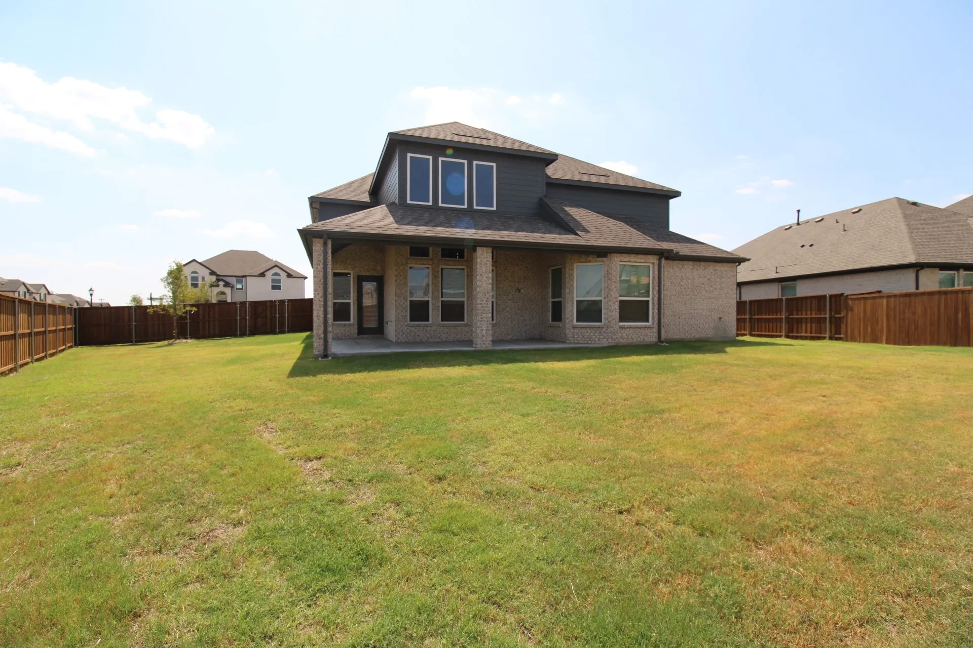 Expansive backyard featuring a manicured lawn, full privacy fencing, and a covered concrete patio