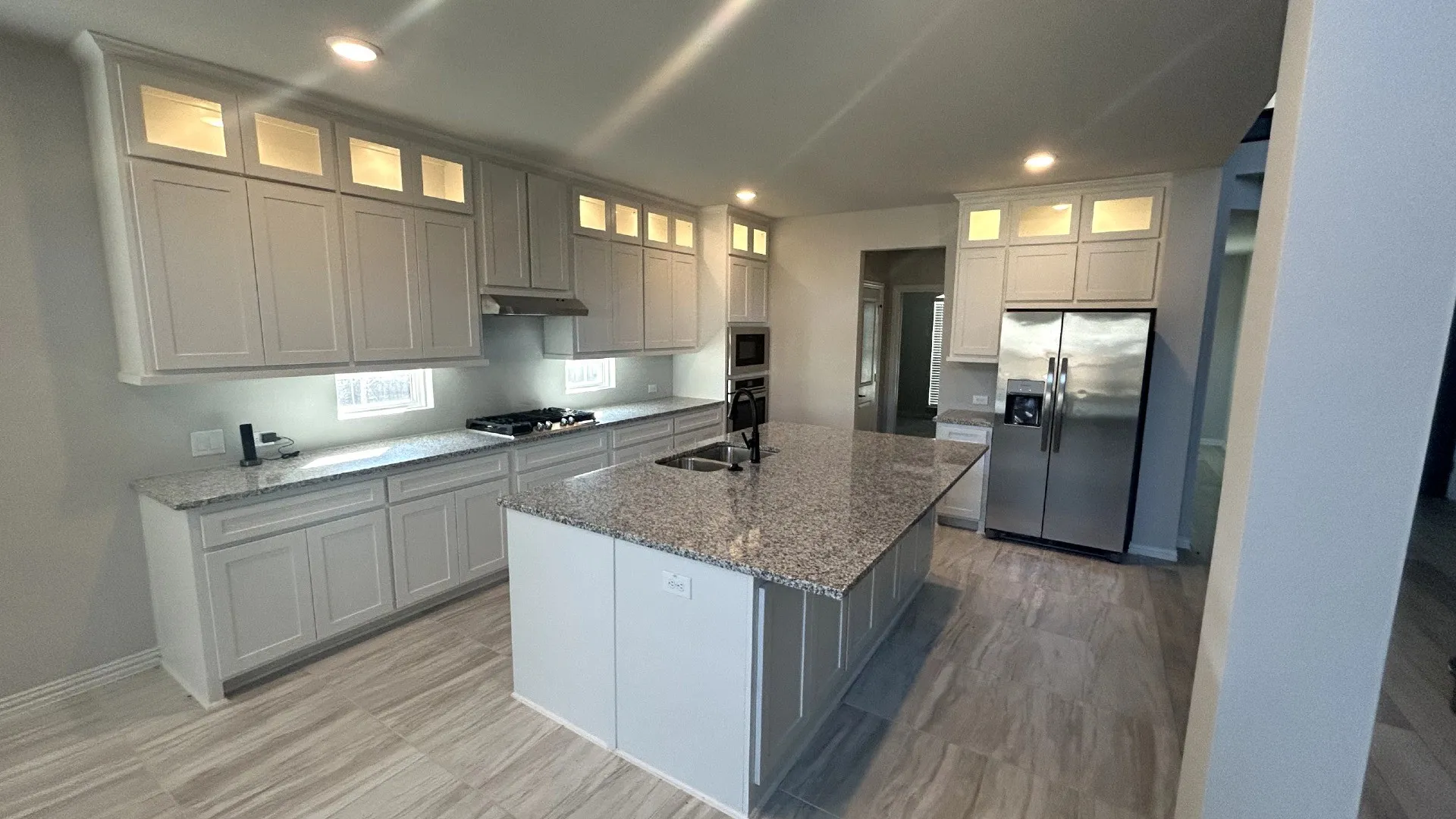 Kitchen featuring light gray cabinetry, granite countertops, a center island with a built-in sink, stainless steel appliances, and wood-finish flooring