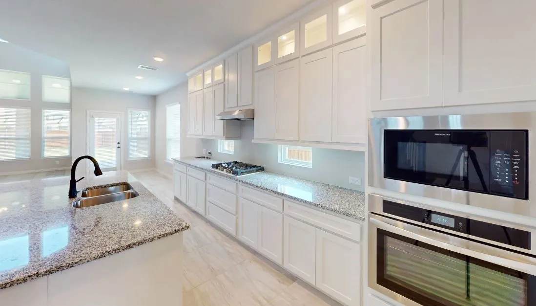 White shaker cabinetry, stainless steel appliances, dual basin sink with gooseneck faucet, light granite countertops, and light tile flooring