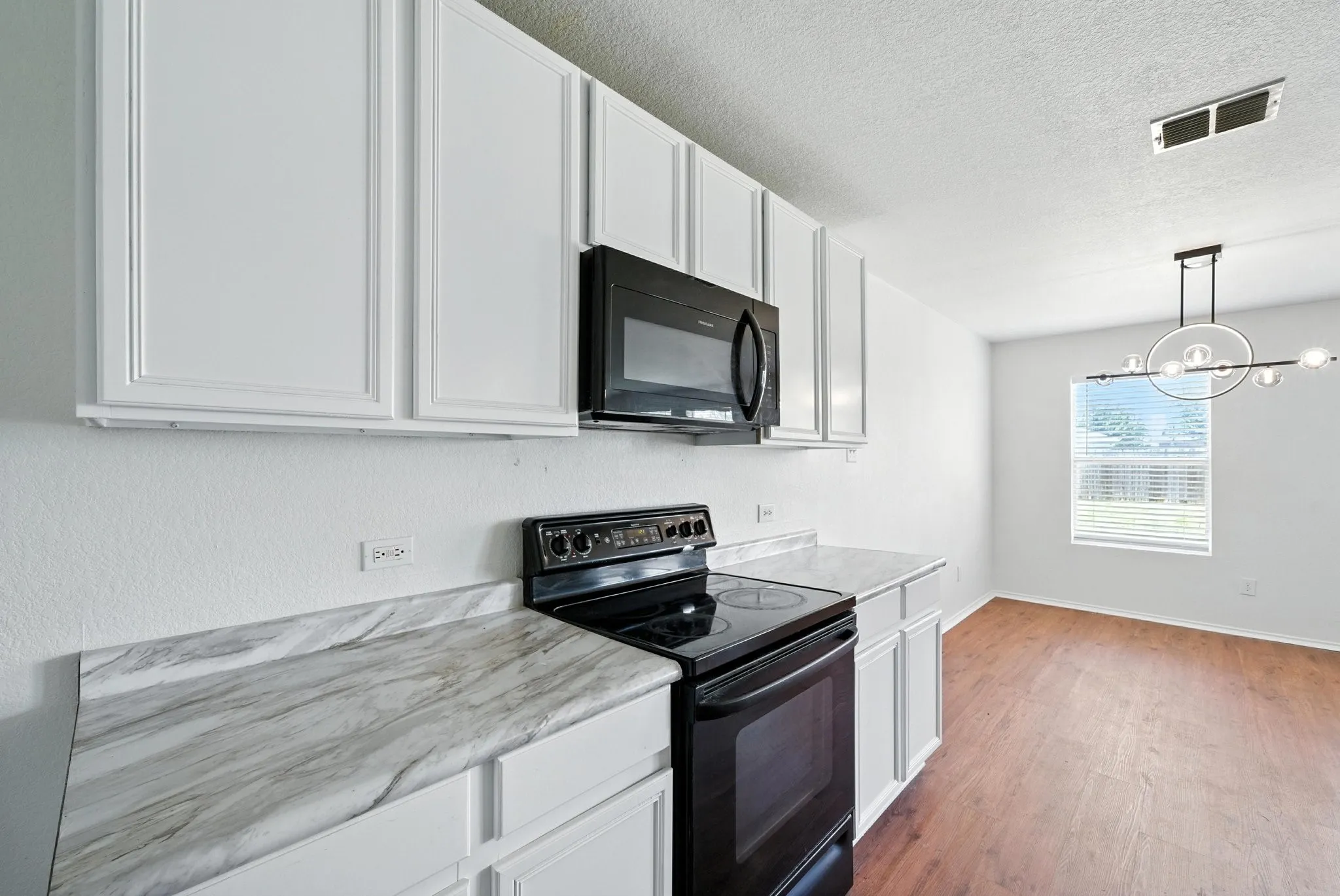 Kitchen with black appliances, white cabinets, light wood-type flooring, a textured ceiling, and a chandelier