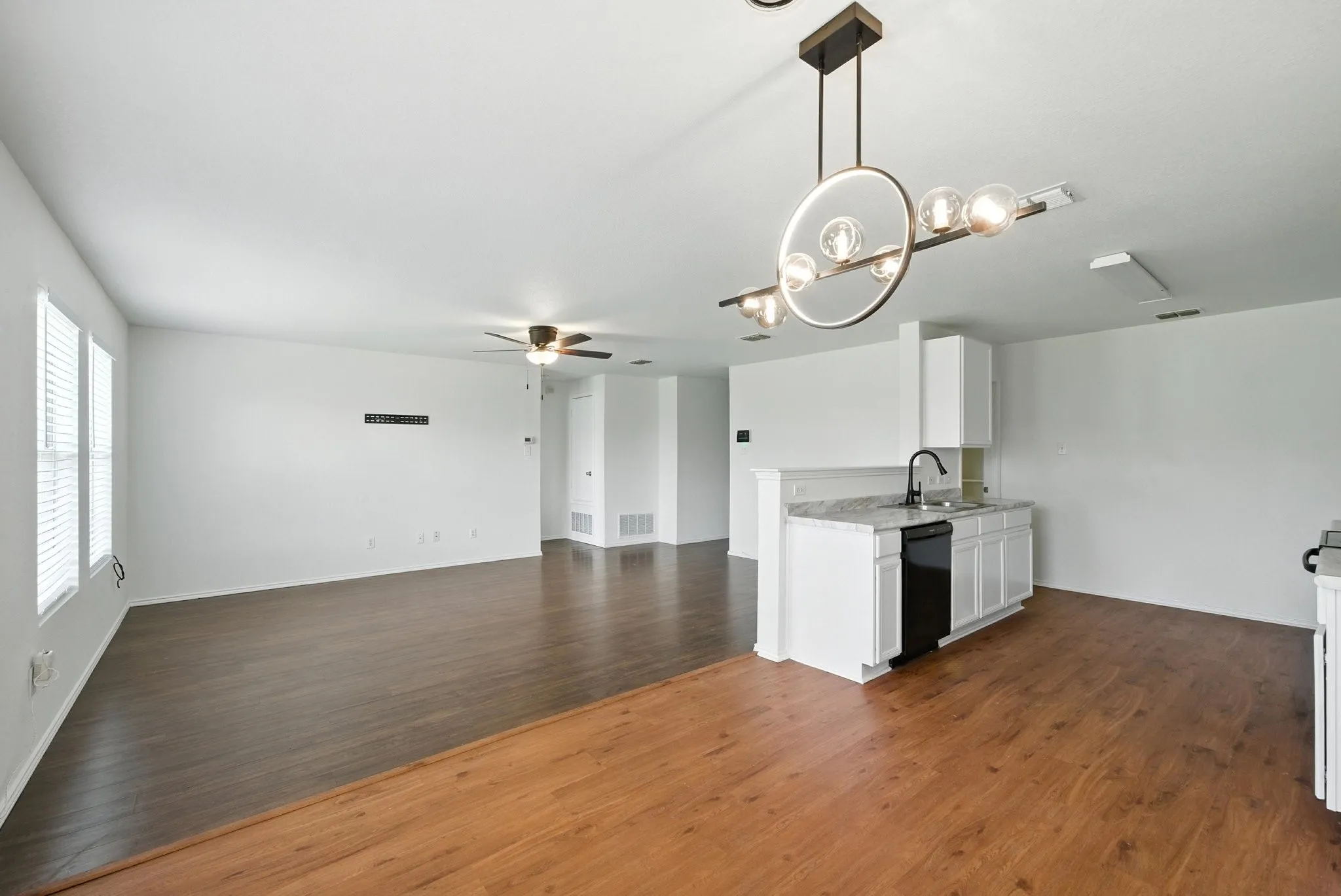 Kitchen with ceiling fan, black dishwasher, white cabinetry, wood finished floors, and a chandelier