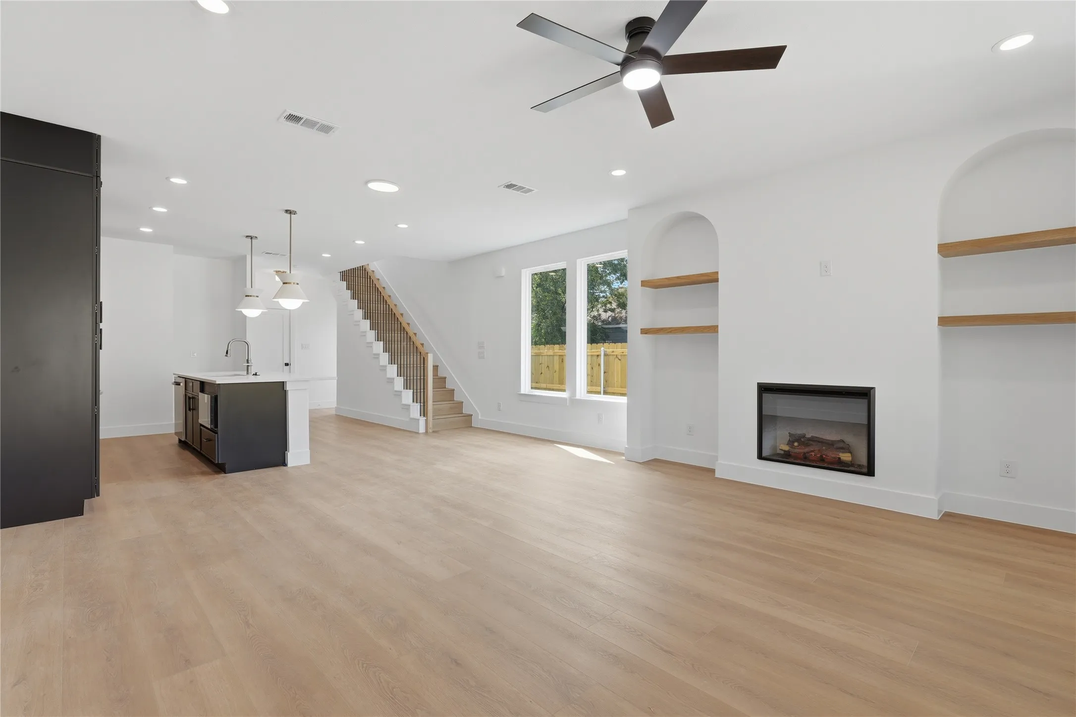 Open-concept living space with light wood-finish flooring, recessed lighting, and a modern fireplace with built-in arched shelving
