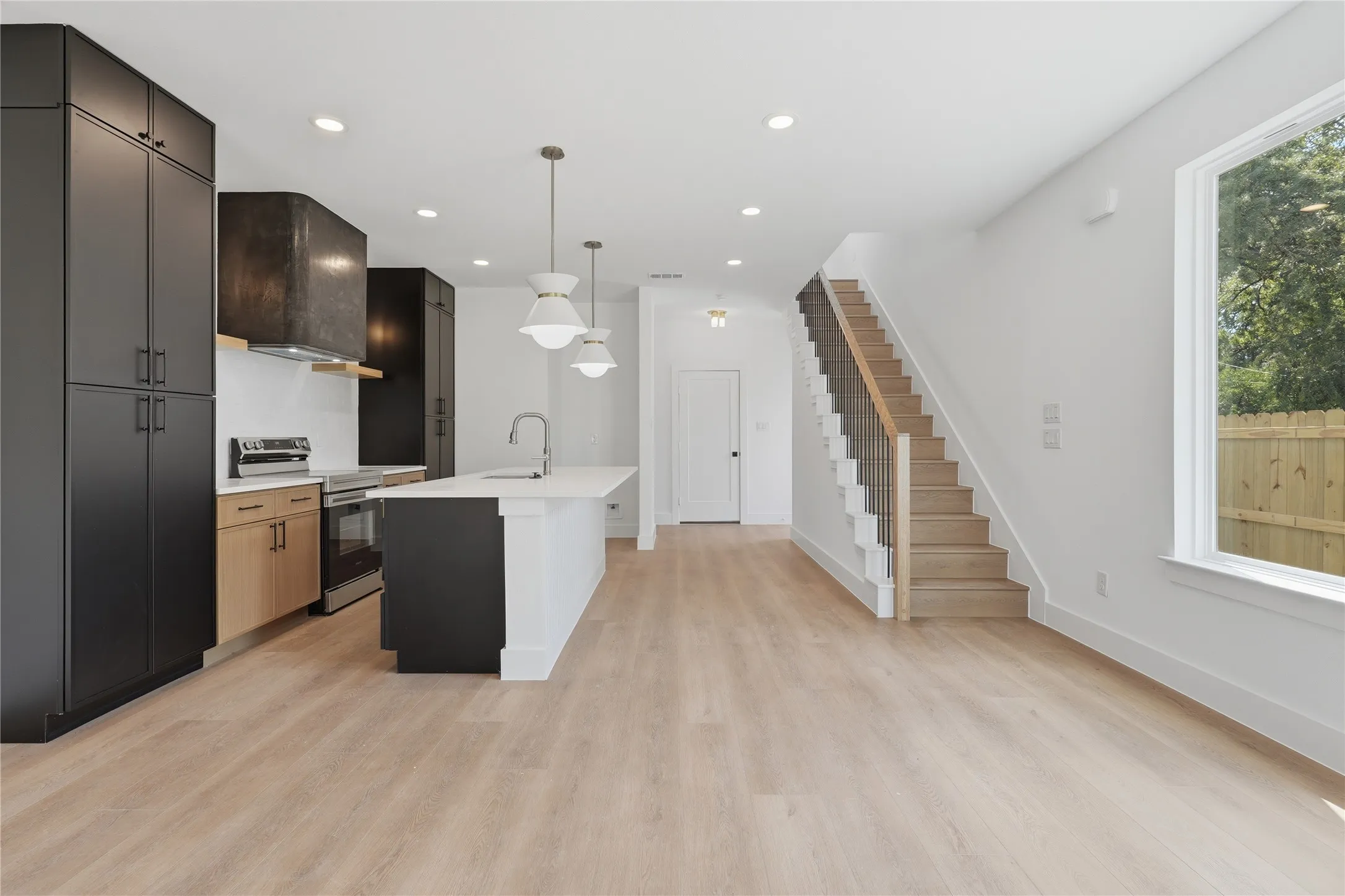Open-concept kitchen with a white island, light wood-finish flooring, and a modern staircase featuring black spindles and a wood handrail