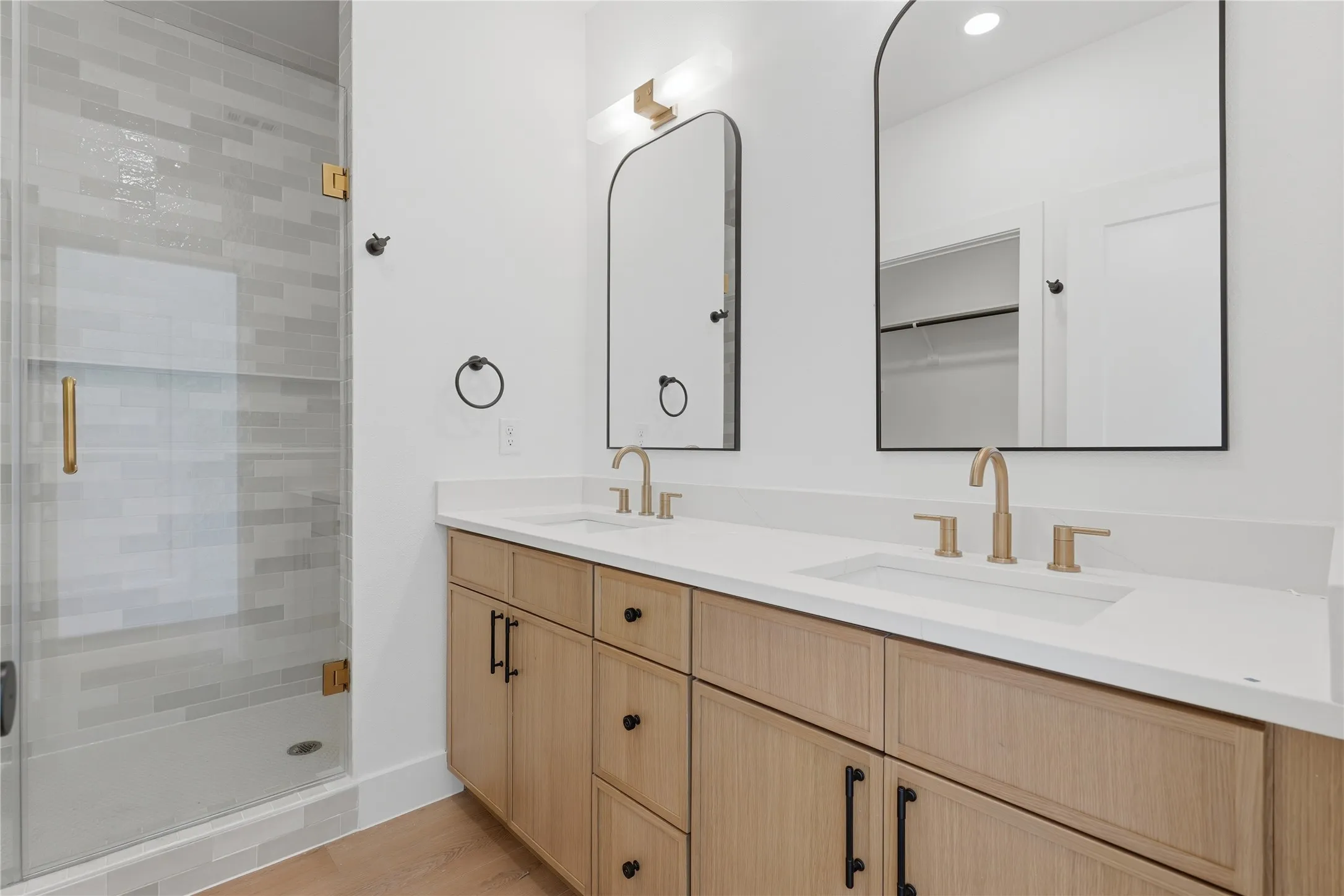 Dual vanity with white countertops, light wood-finish cabinetry, and gold-finish fixtures