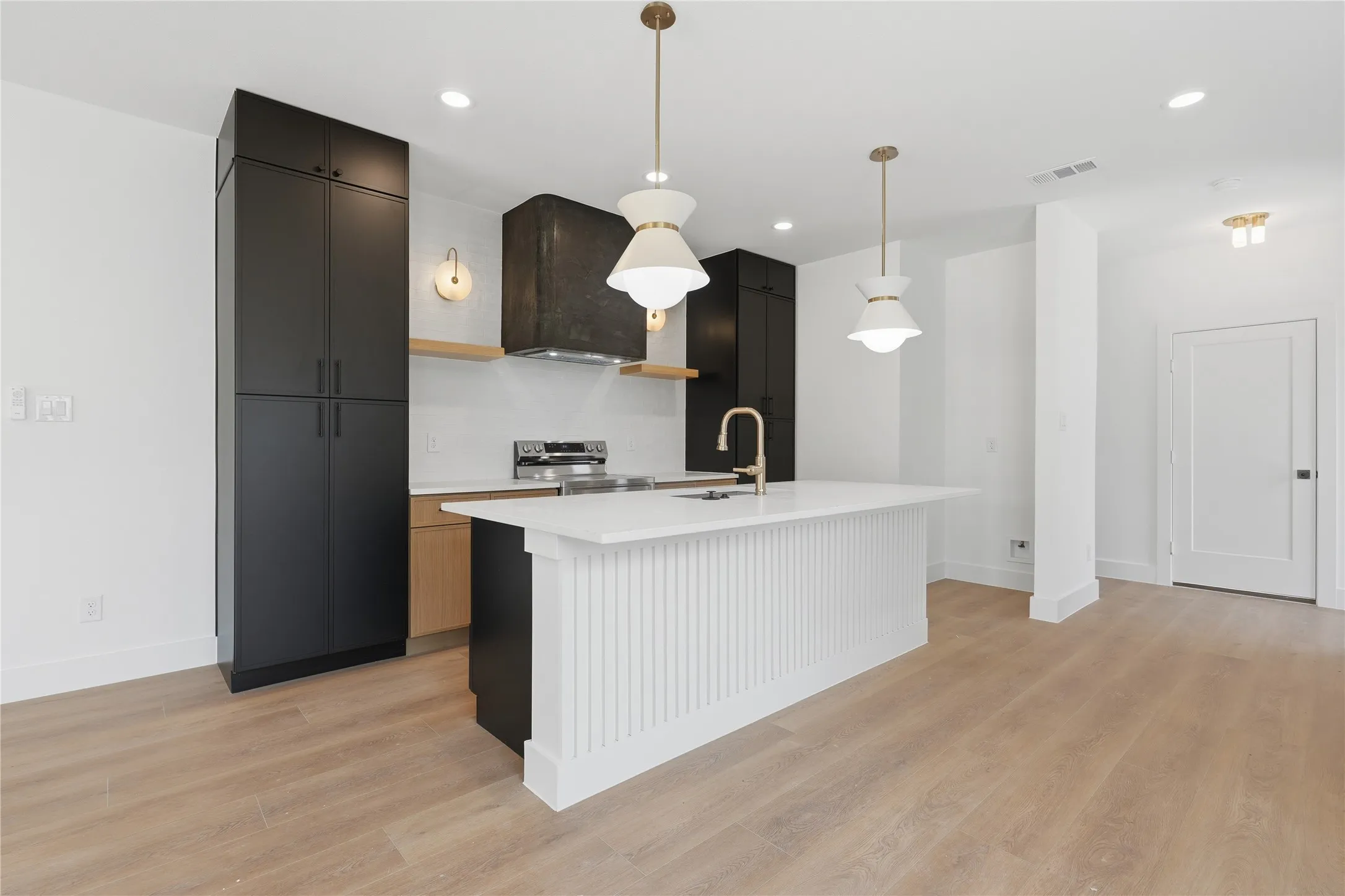 Modern kitchen featuring a large center island with fluted paneling, light wood-finish flooring, matte black cabinetry, and gold-tone pendant lighting