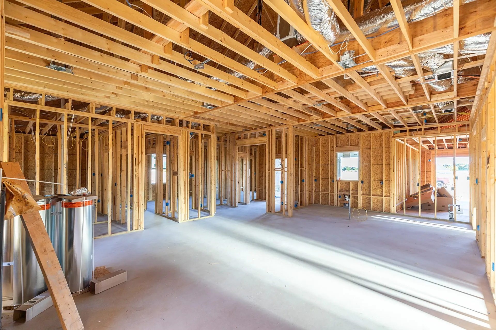 New construction framing with exposed ceiling joists, multiple framed interior walls, and visible window openings