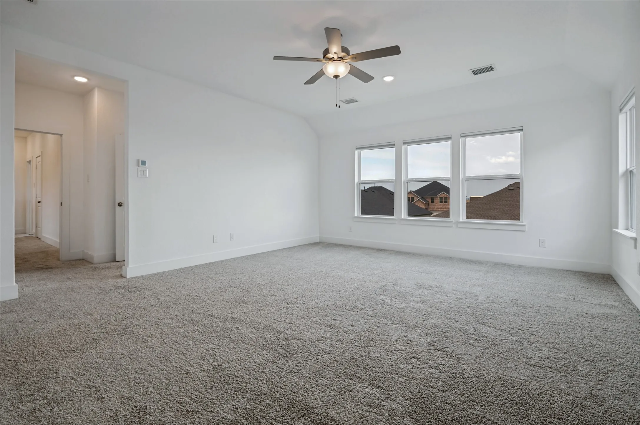 Expansive room featuring clean white walls, plush gray carpeting, three large windows, and a ceiling fan with integrated lighting