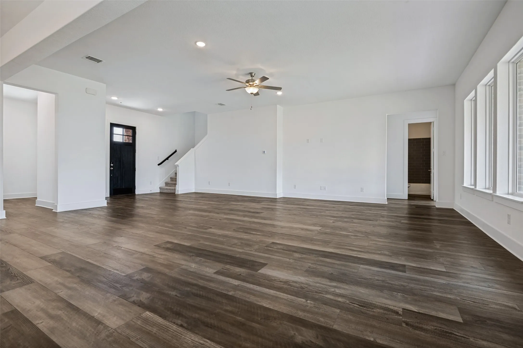 Spacious interior with wood-finish flooring, multiple windows providing natural light, a ceiling fan, and a prominent staircase