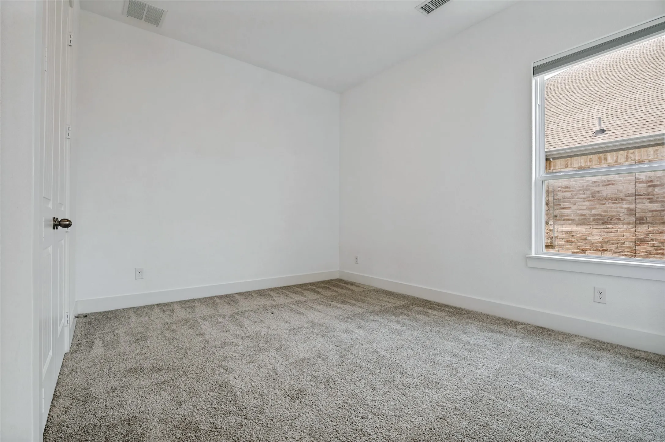 White walls and gray carpeting, featuring a single window and a white panel door with dark hardware