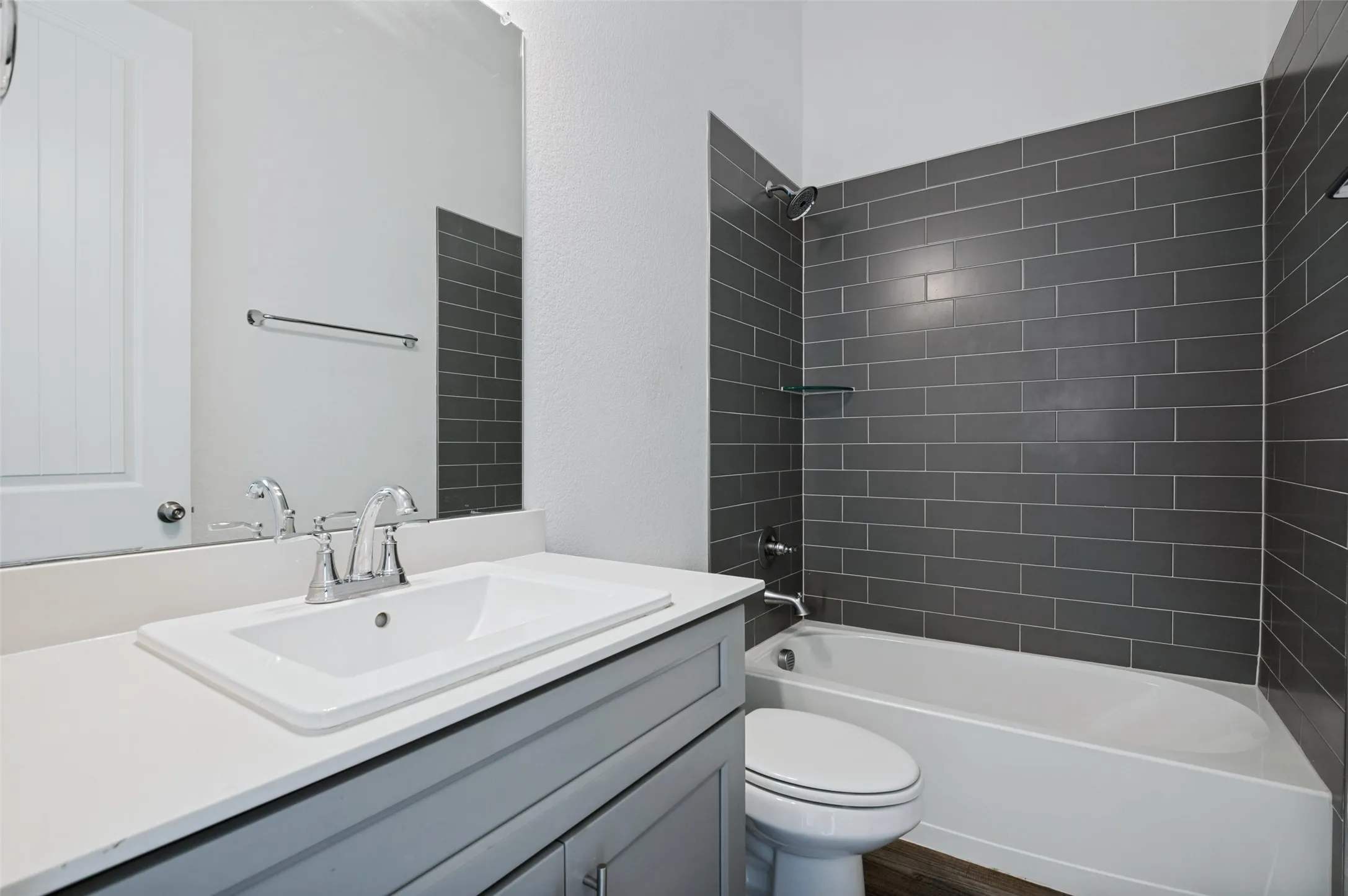 Bathroom featuring a vanity with a rectangular undermount sink, a white countertop, and a shower-over-tub combination with dark subway tile surround