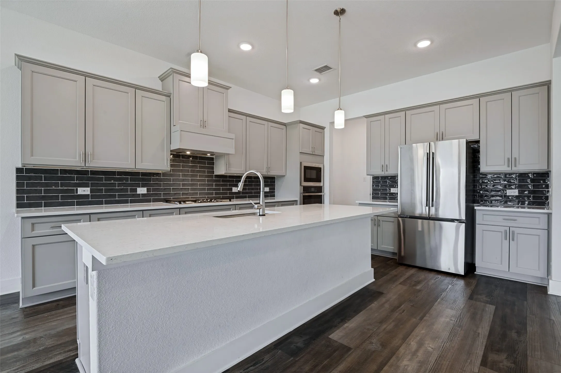 Kitchen featuring a center island, stainless steel appliances, dark subway tile backsplash, light gray cabinetry, and wood-finish flooring