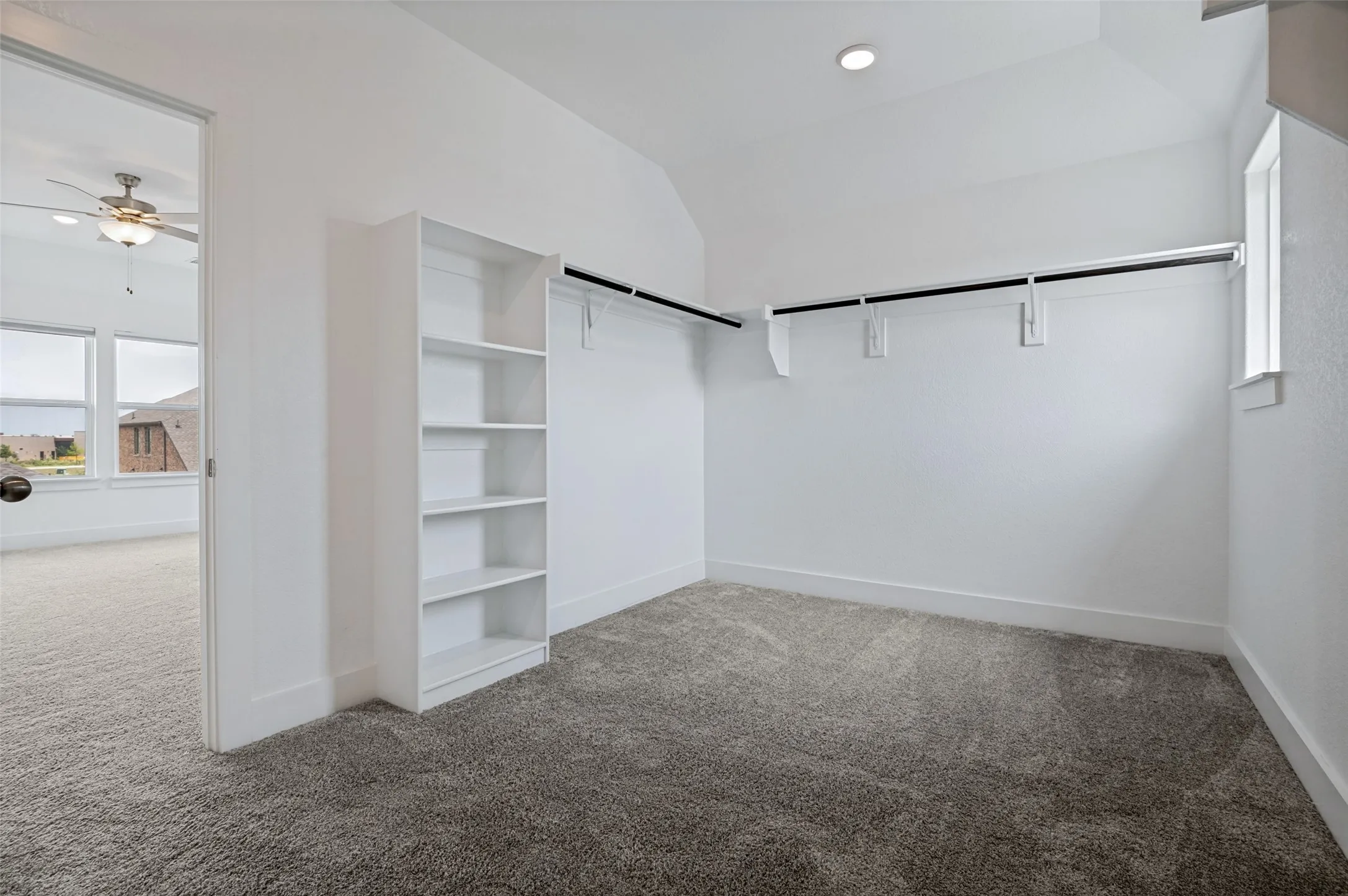 White built-in shelving, mounted clothing rods, recessed ceiling lighting, and grey carpet flooring