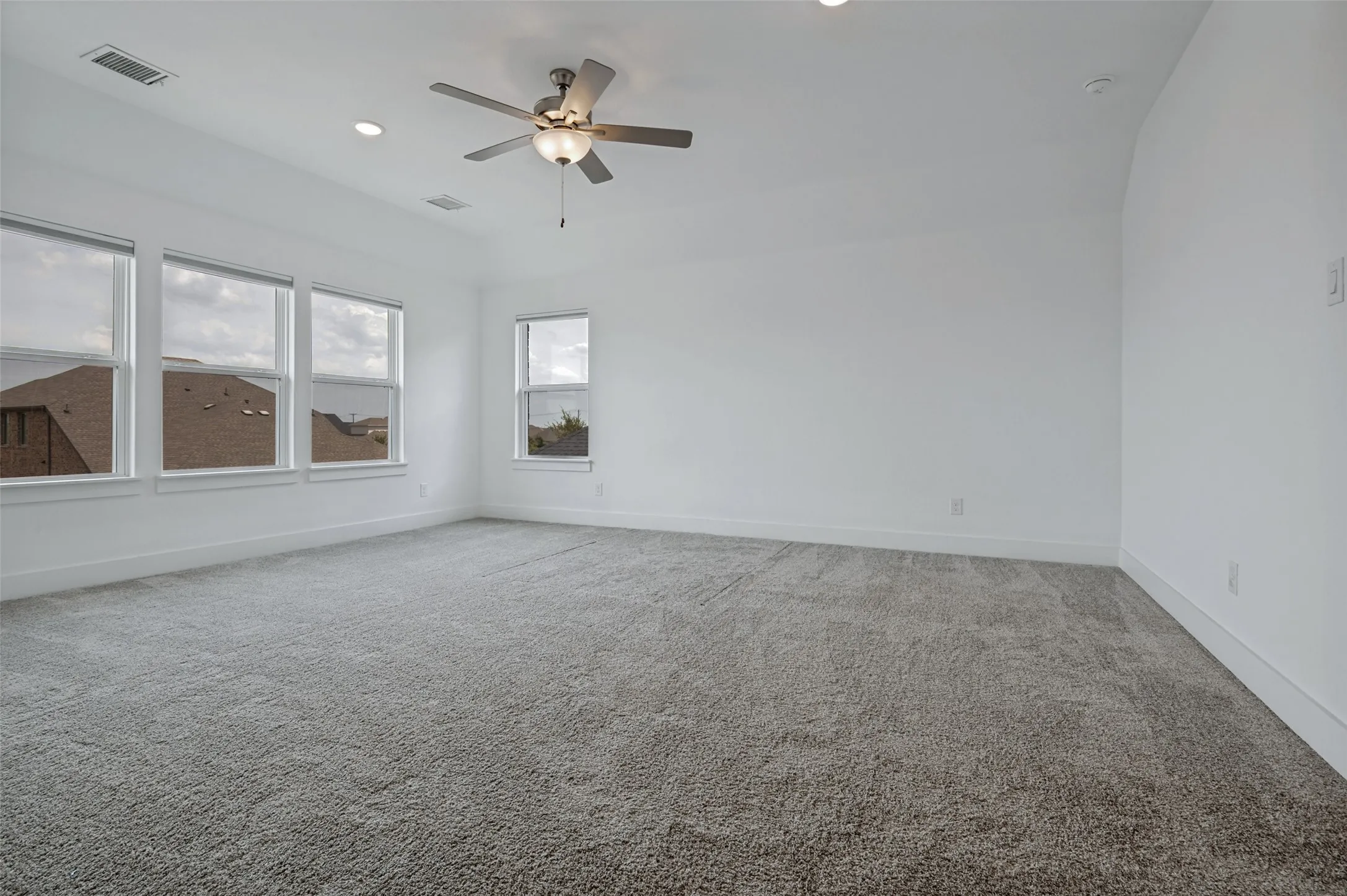 Spacious room featuring neutral carpeting, multiple windows, recessed lighting, and a ceiling fan