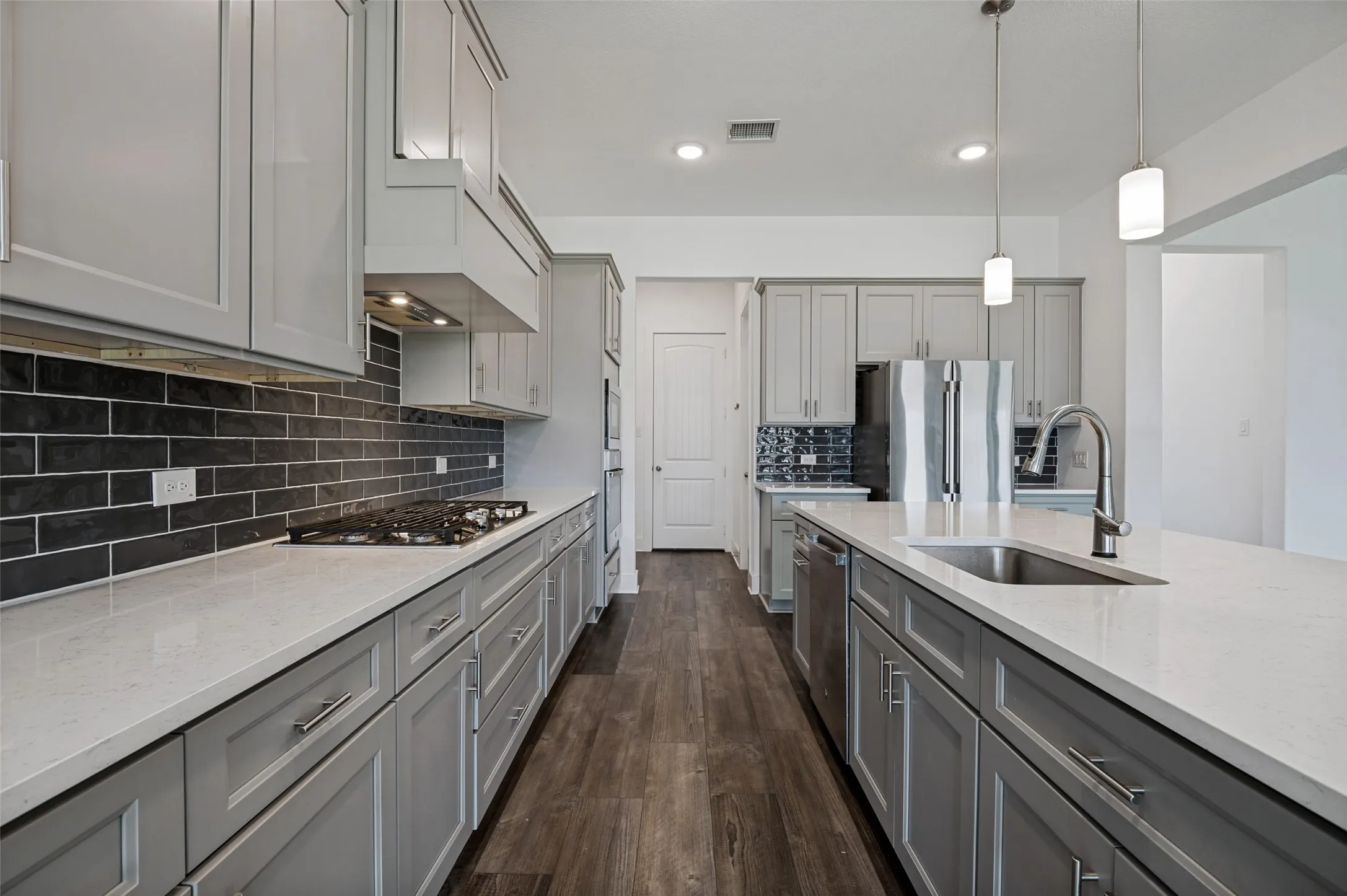 Modern kitchen featuring light gray cabinetry, light-colored countertops, dark subway tile backsplash, a stainless-steel sink with a gooseneck faucet, and wood-finish flooring