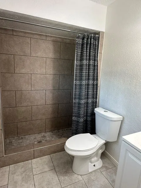 Built-in shower with large format wall tiles, mosaic tile shower pan, and a white toilet