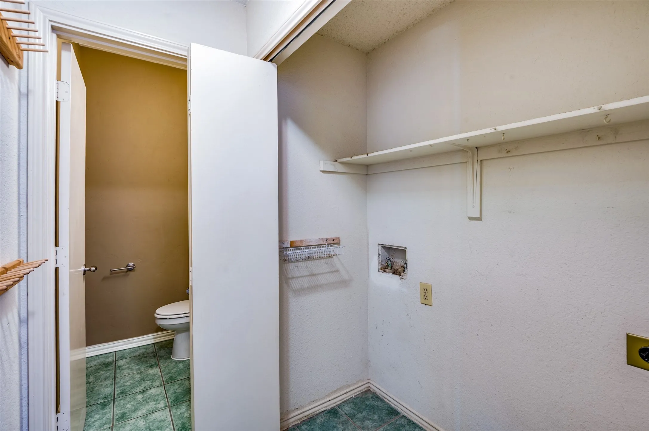 Utility area with wall-mounted shelving and a half-bath featuring green tiled flooring
