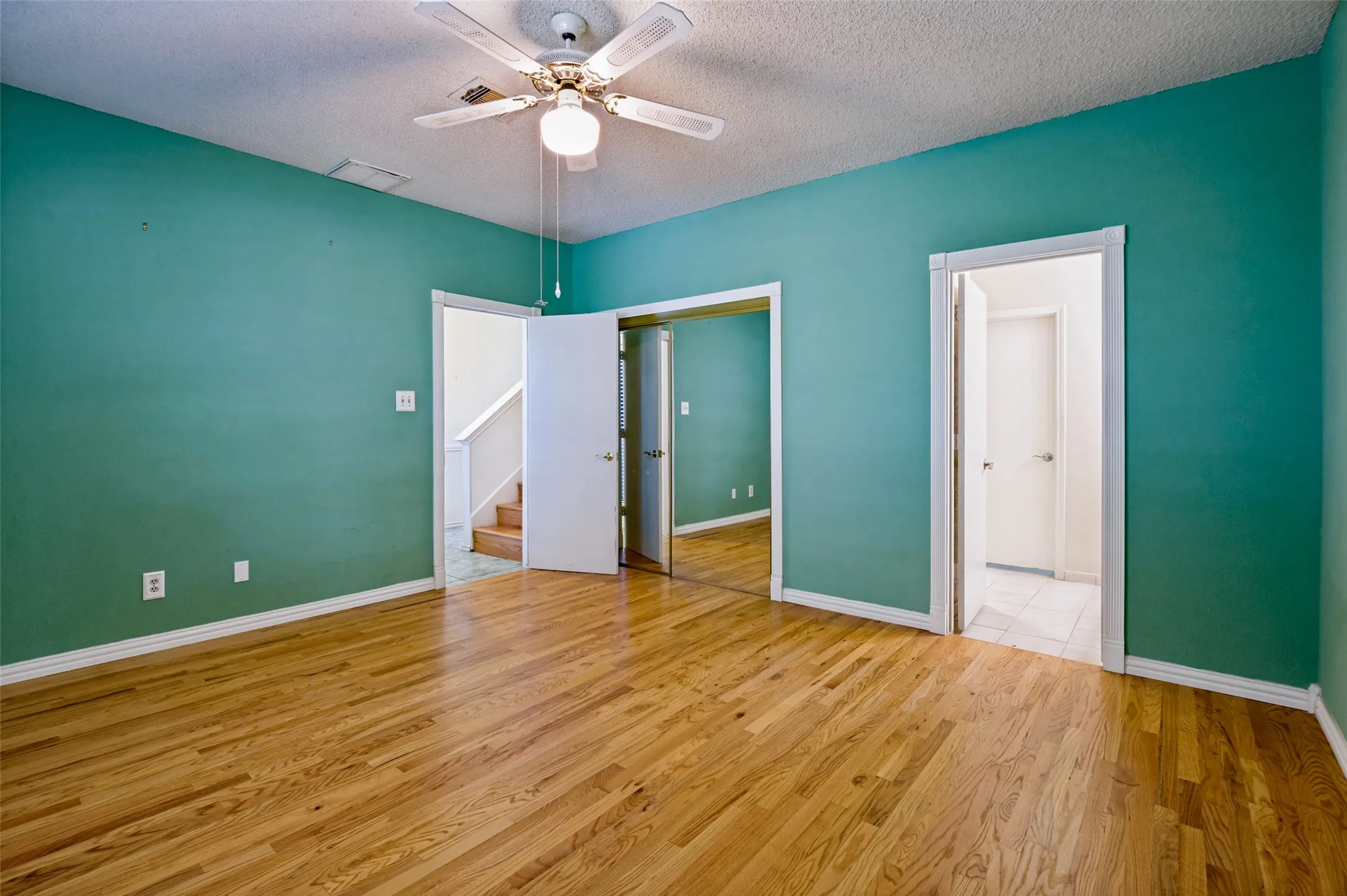 Wood-finish flooring, ceiling fan with integrated lighting, and multiple doorways providing access to additional areas