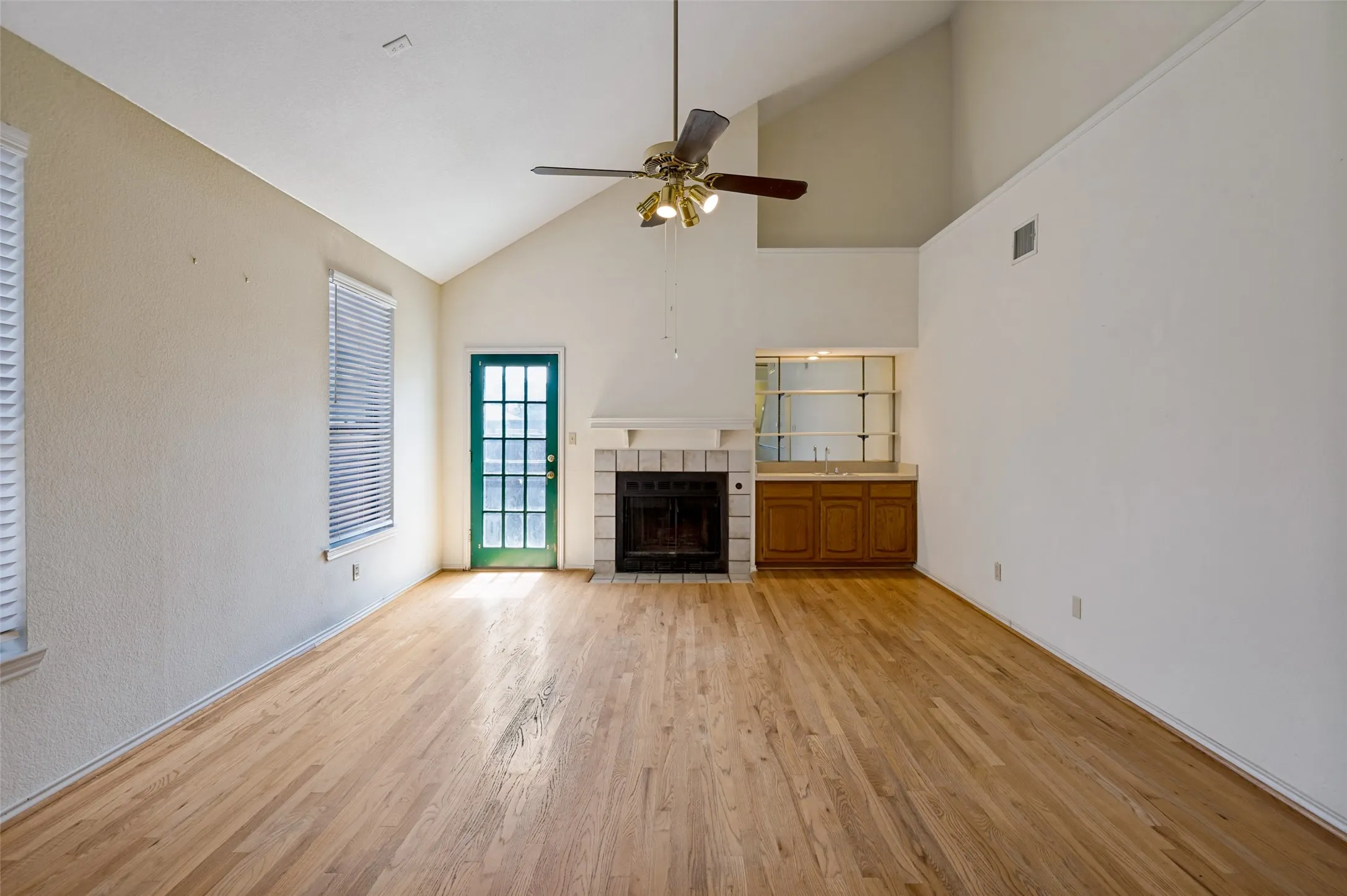 Vaulted ceiling with a ceiling fan, wood-finish flooring, fireplace with a tile surround, built-in wet bar with mirrored shelving, and a glass-paned door