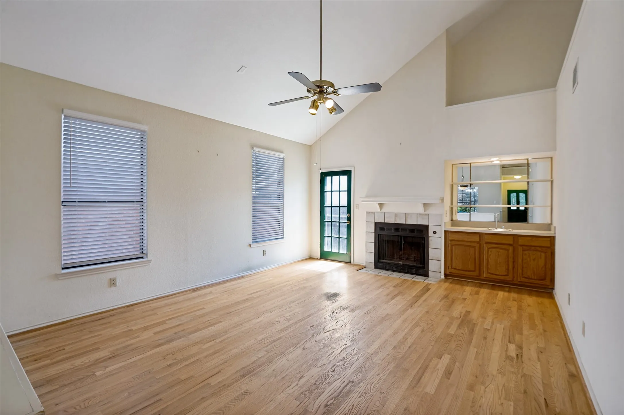 Hardwood-finish flooring, vaulted ceiling, fireplace with tile surround, built-in wet bar with wood cabinetry, and ceiling fan