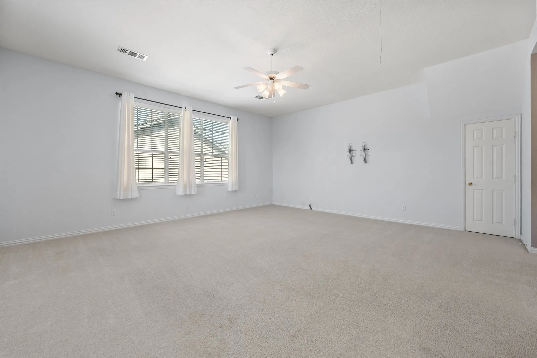 Spacious gameroom featuring light-colored carpeting, a ceiling fan, and the door to the walk in attic