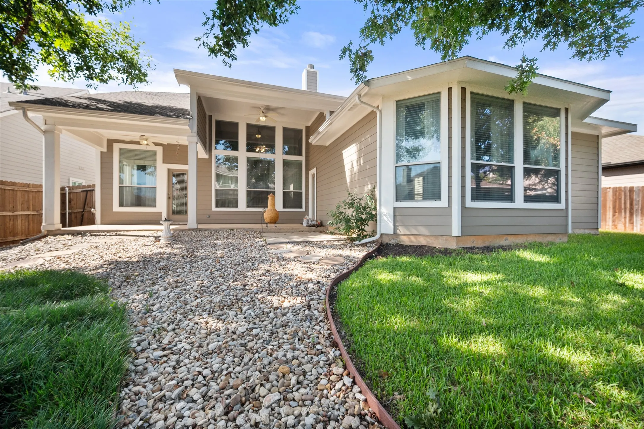 Covered patio with ceiling fans, concrete patio surface, bay windows, gravel pathway, and manicured lawn