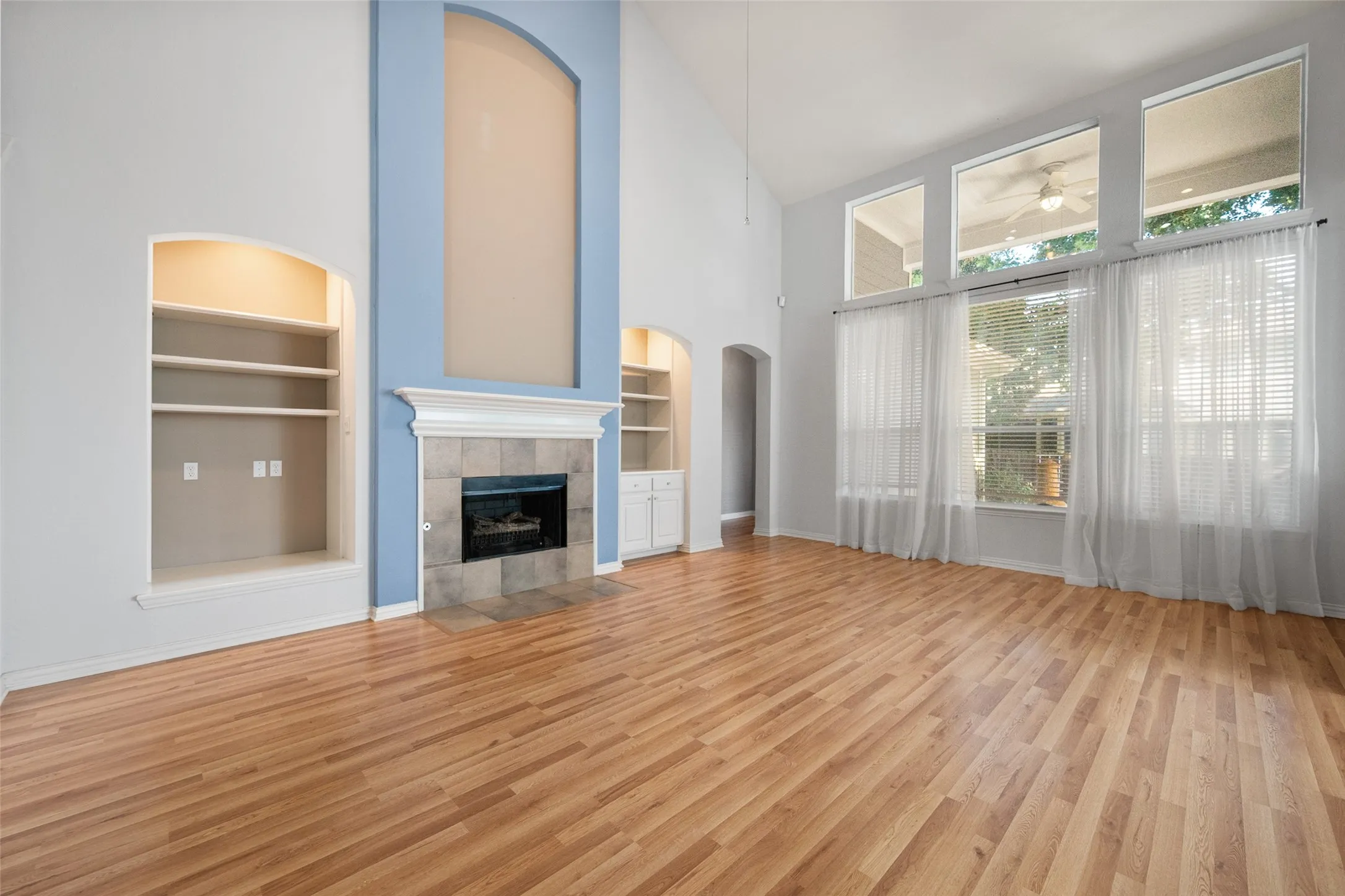 Wood-finish flooring, a fireplace with a tile surround and decorative mantel, built-in shelving, high vaulted ceilings, and large windows