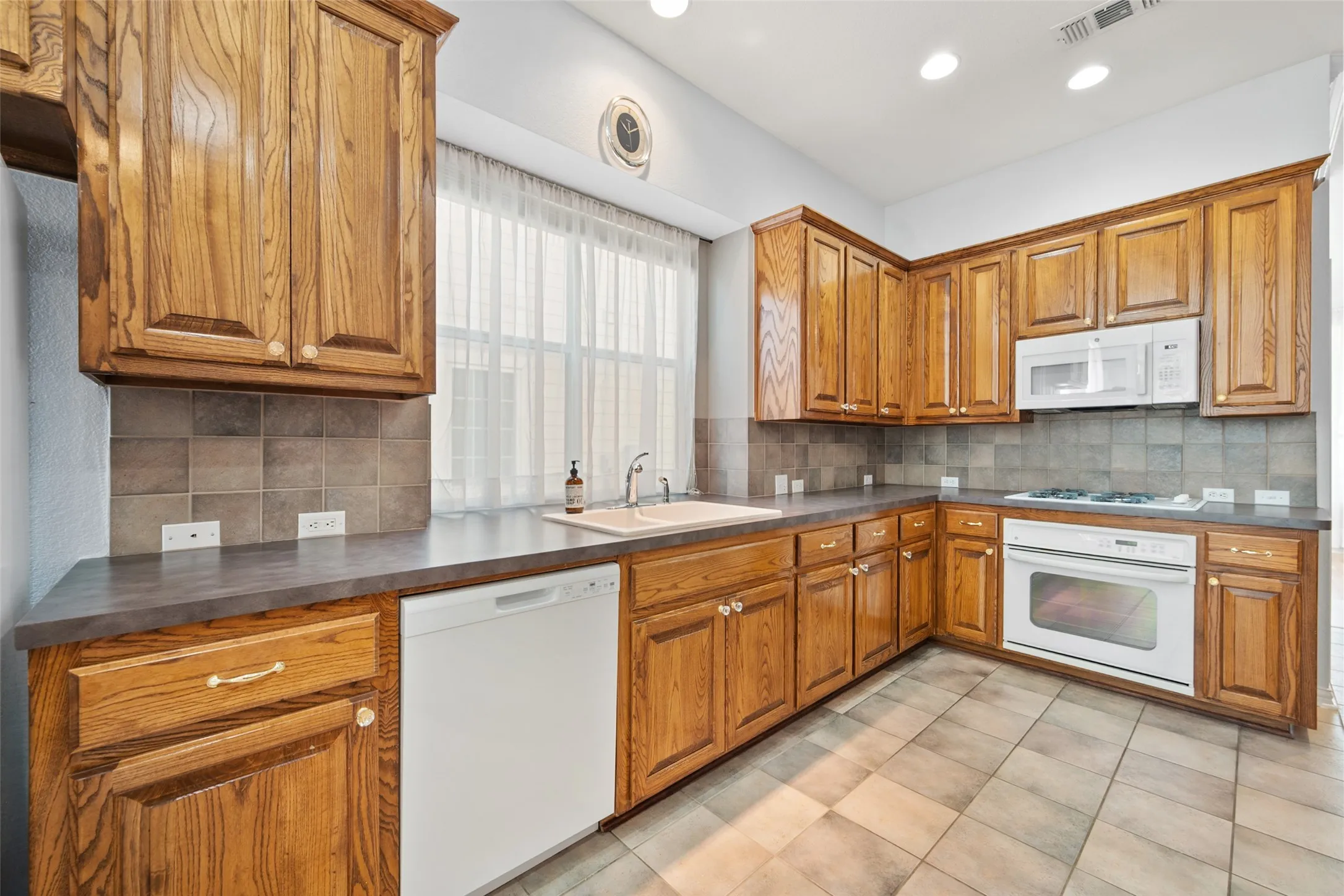 Kitchen featuring wood-finish cabinetry, tile backsplash, built-in microwave, integrated oven, and tile flooring