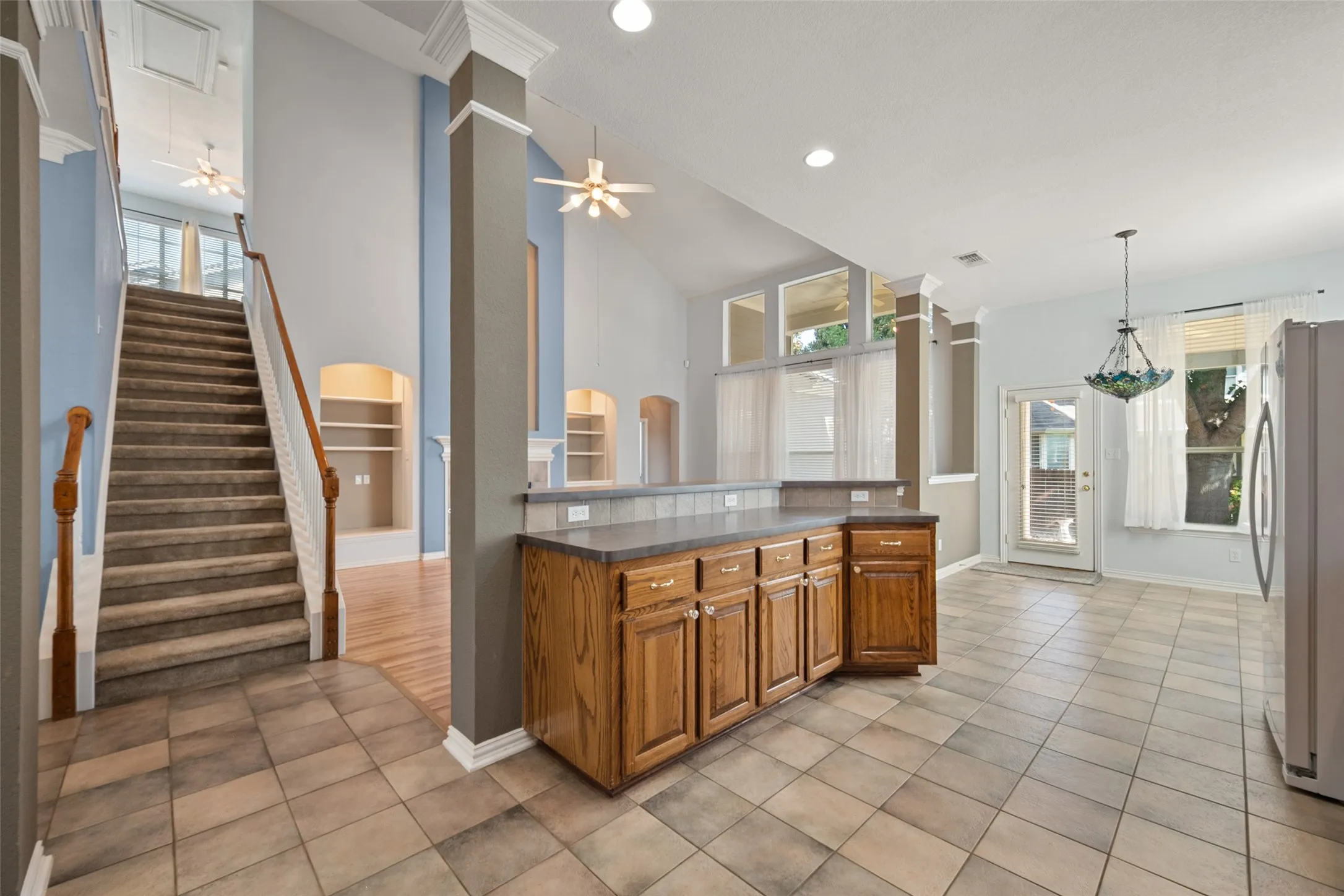 Tiled flooring throughout, built-in custom cabinetry, staircase with wooden banister, vaulted ceiling, and built-in shelving