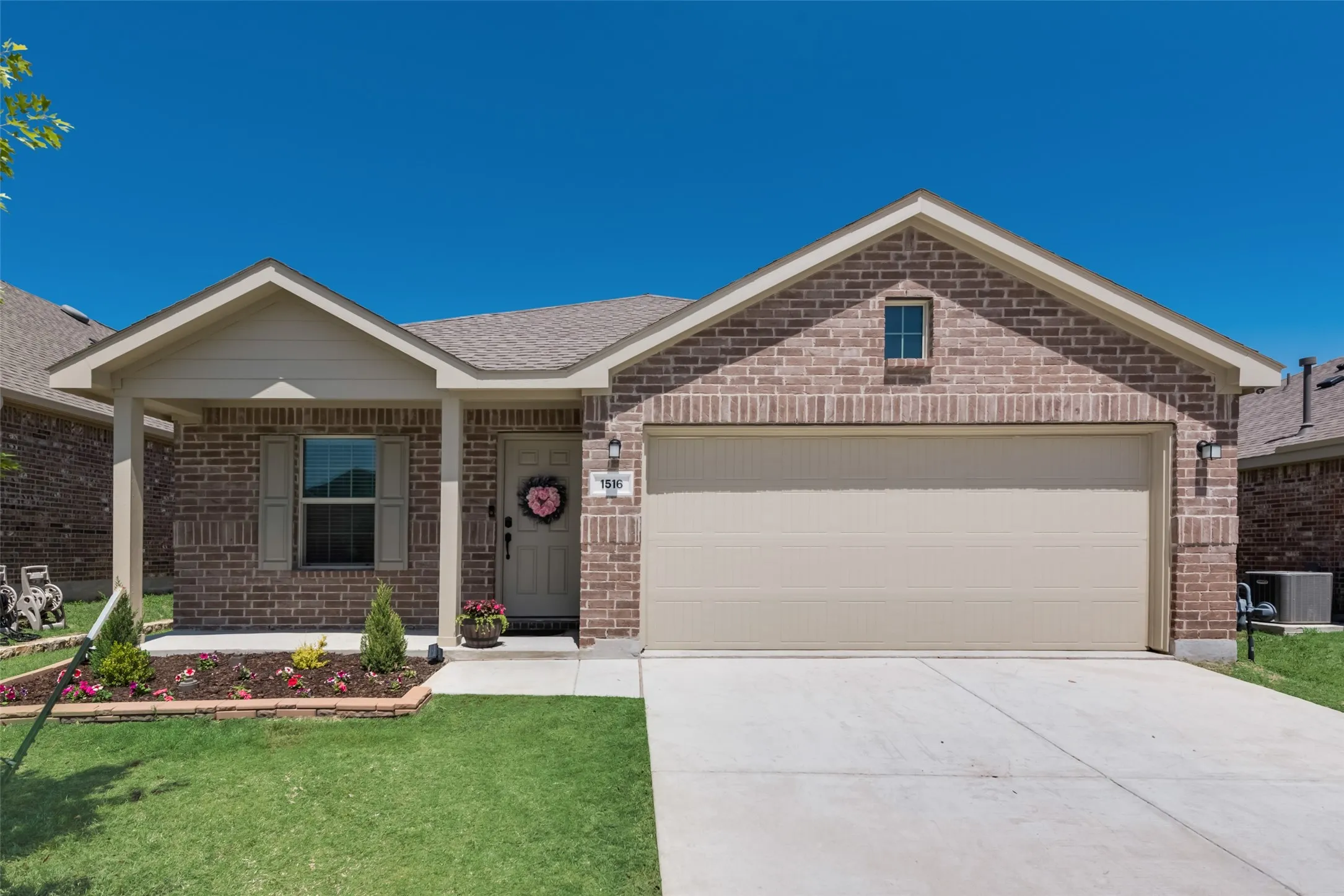 Brick exterior with a covered porch, attached garage, and landscaped front yard