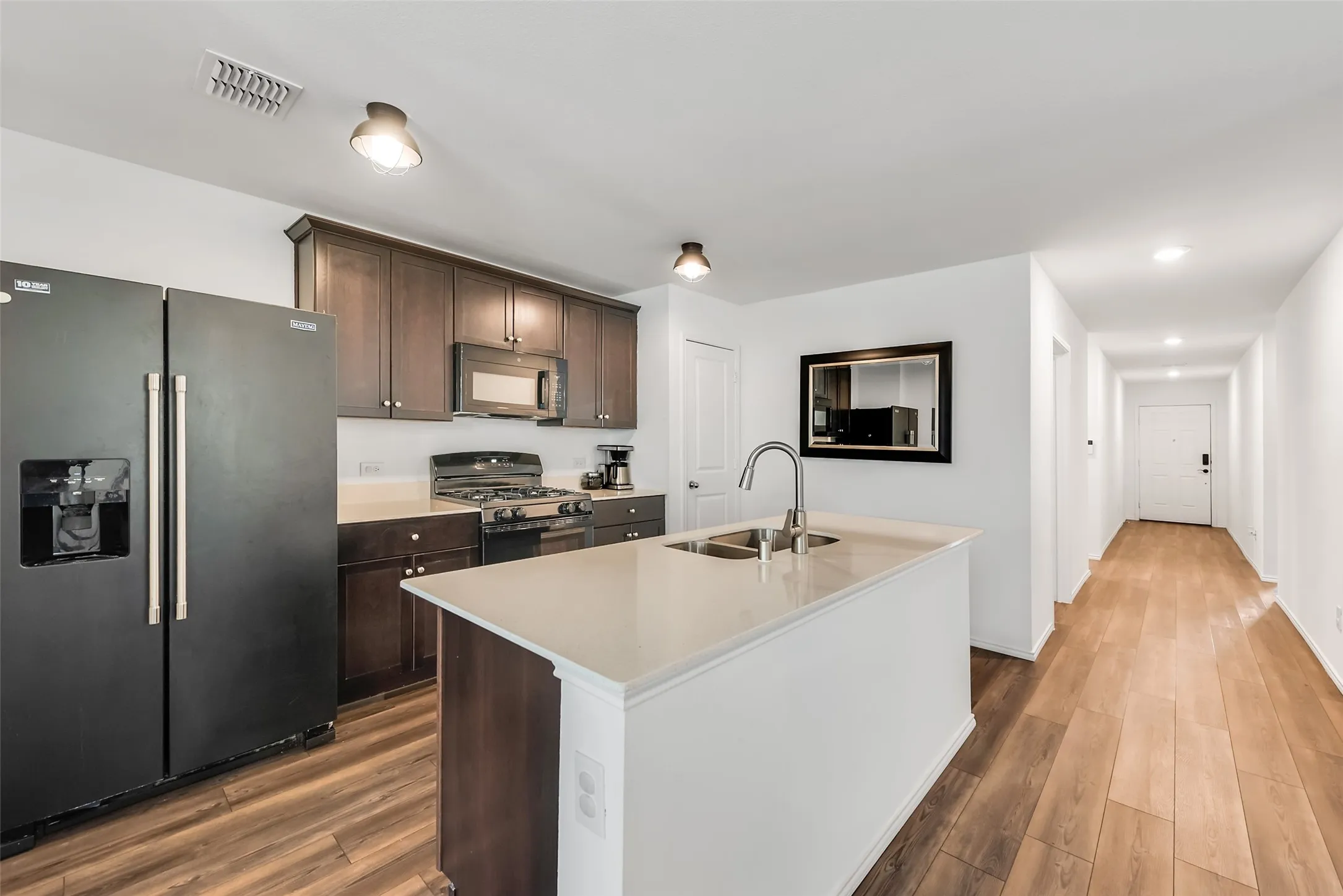 Kitchen featuring wood-finish flooring, dark wood cabinetry, a center island with a sink, and a black appliance package