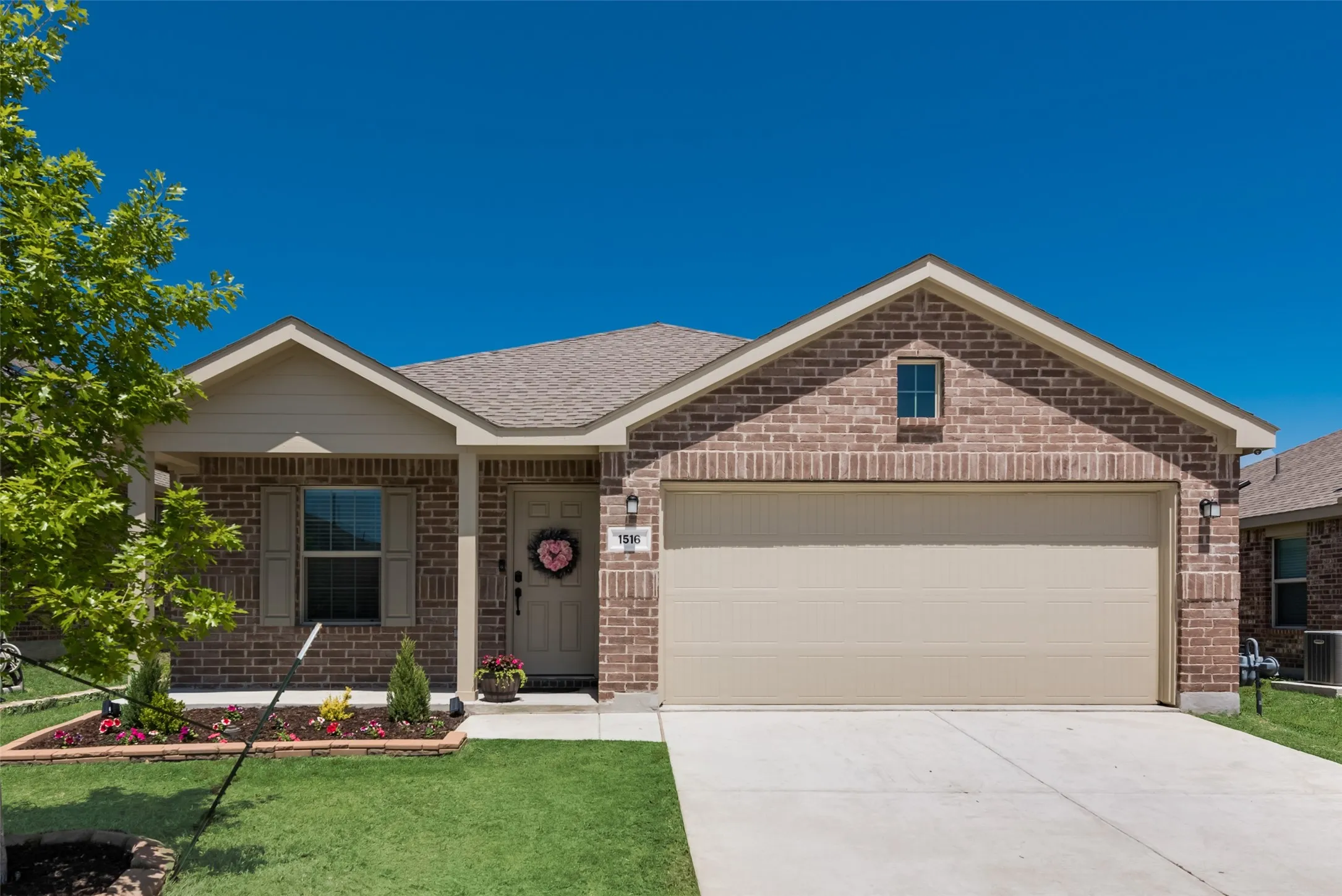 Brick facade with a neutral-toned garage door, concrete driveway, and covered entry